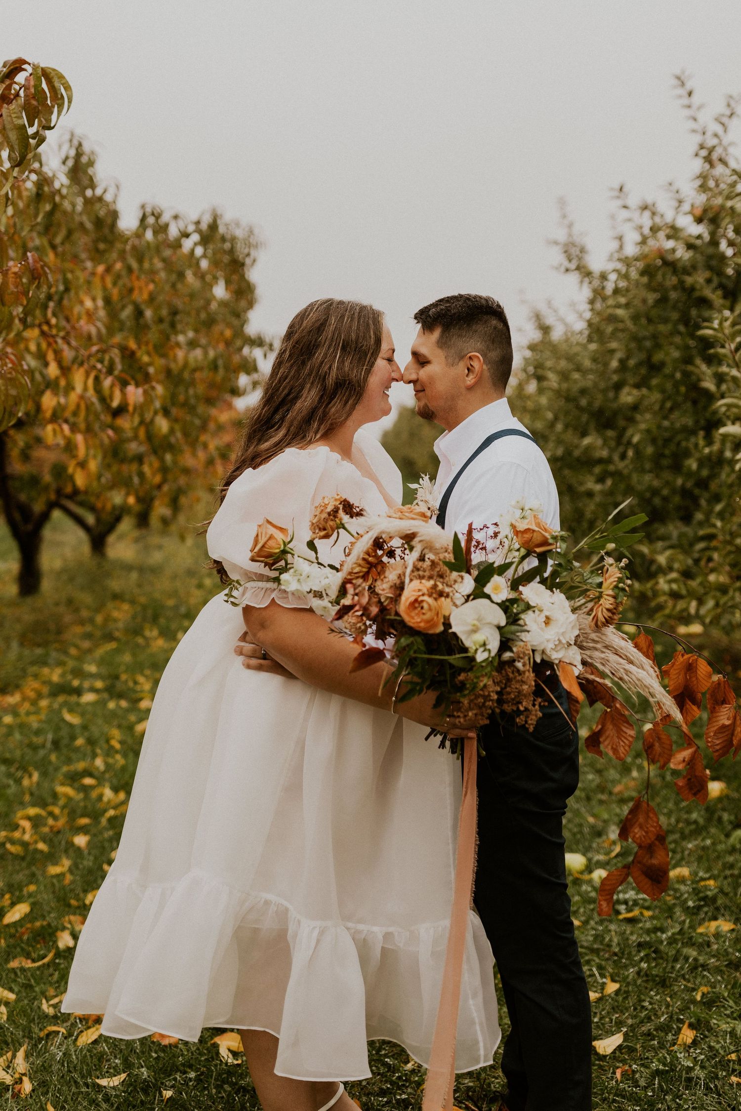 Terise and Jose kissing in between the rows of apple trees at Carter Hill Orchard in Concord New Hampshire]