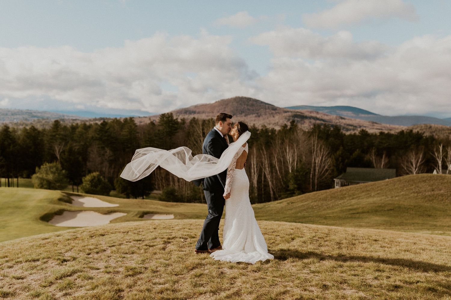 Husband and wife embracing each other and kissing with a view of the white mountains in the background.