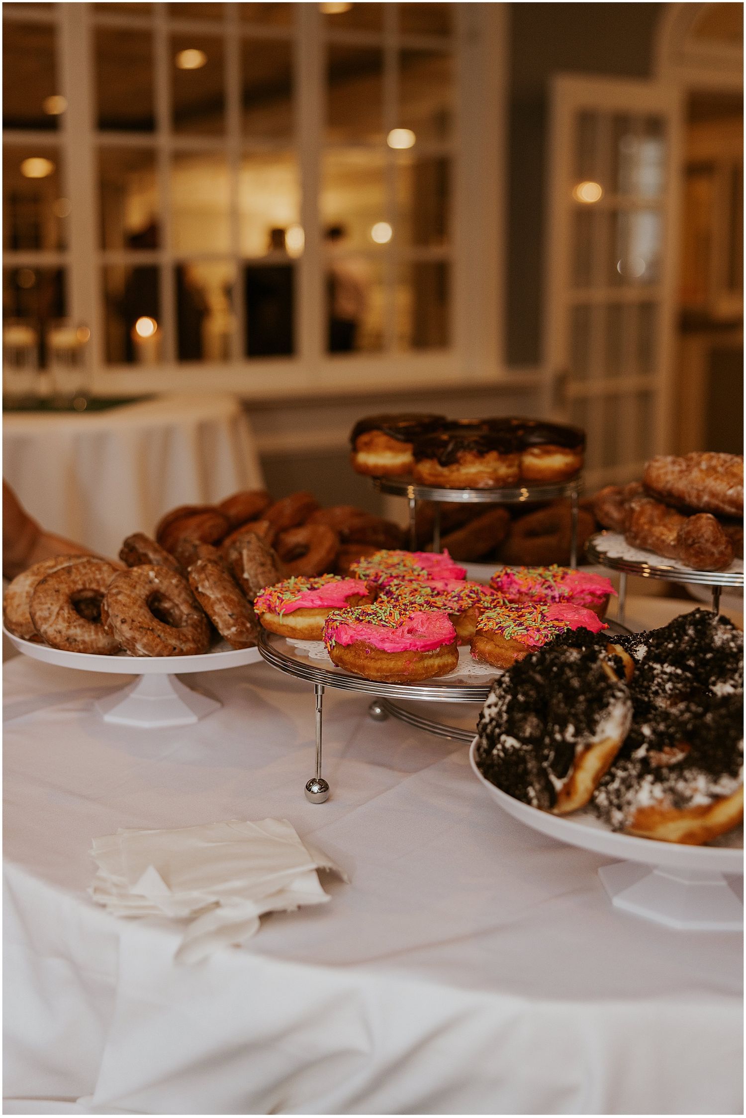Assorted donuts on white cake stands at a wedding dessert table.