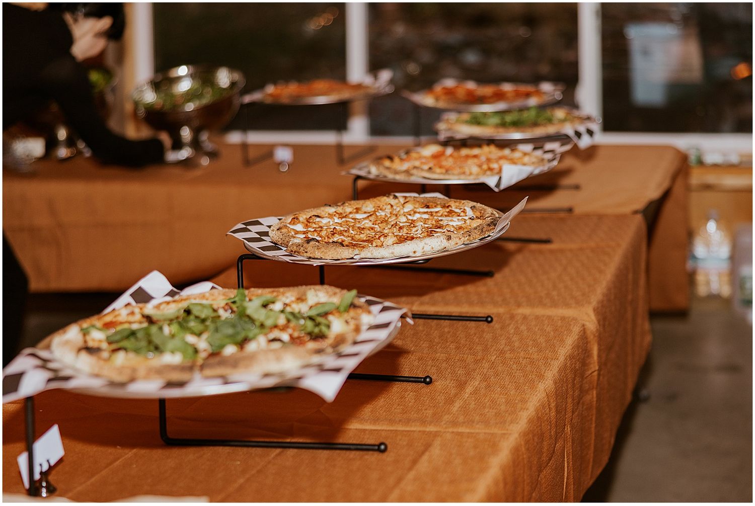 Pizza slices arranged on serving platters across a long buffet table.