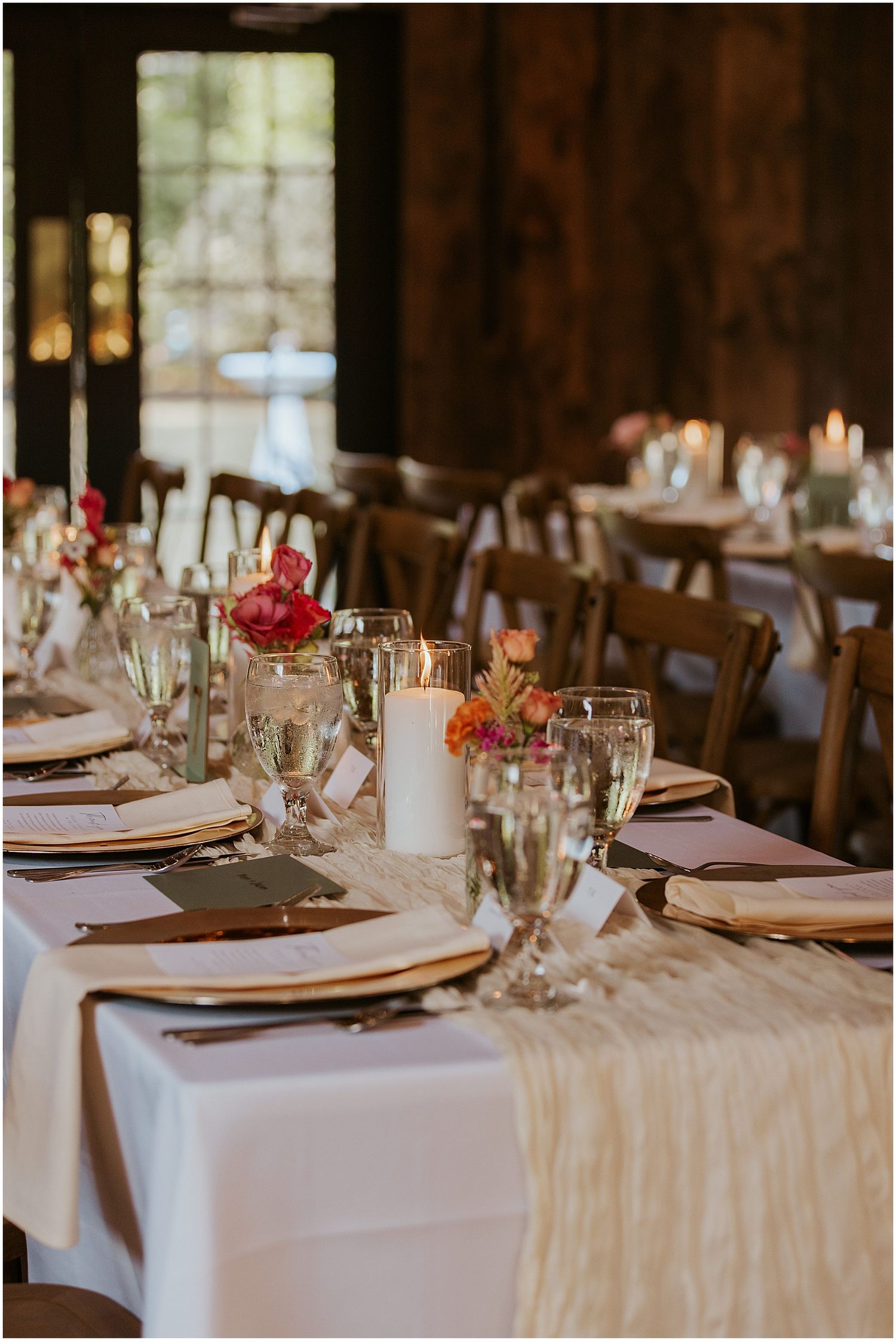 Elegant wedding reception tables set with white linens, candles and floral centerpieces in a rustic barn.