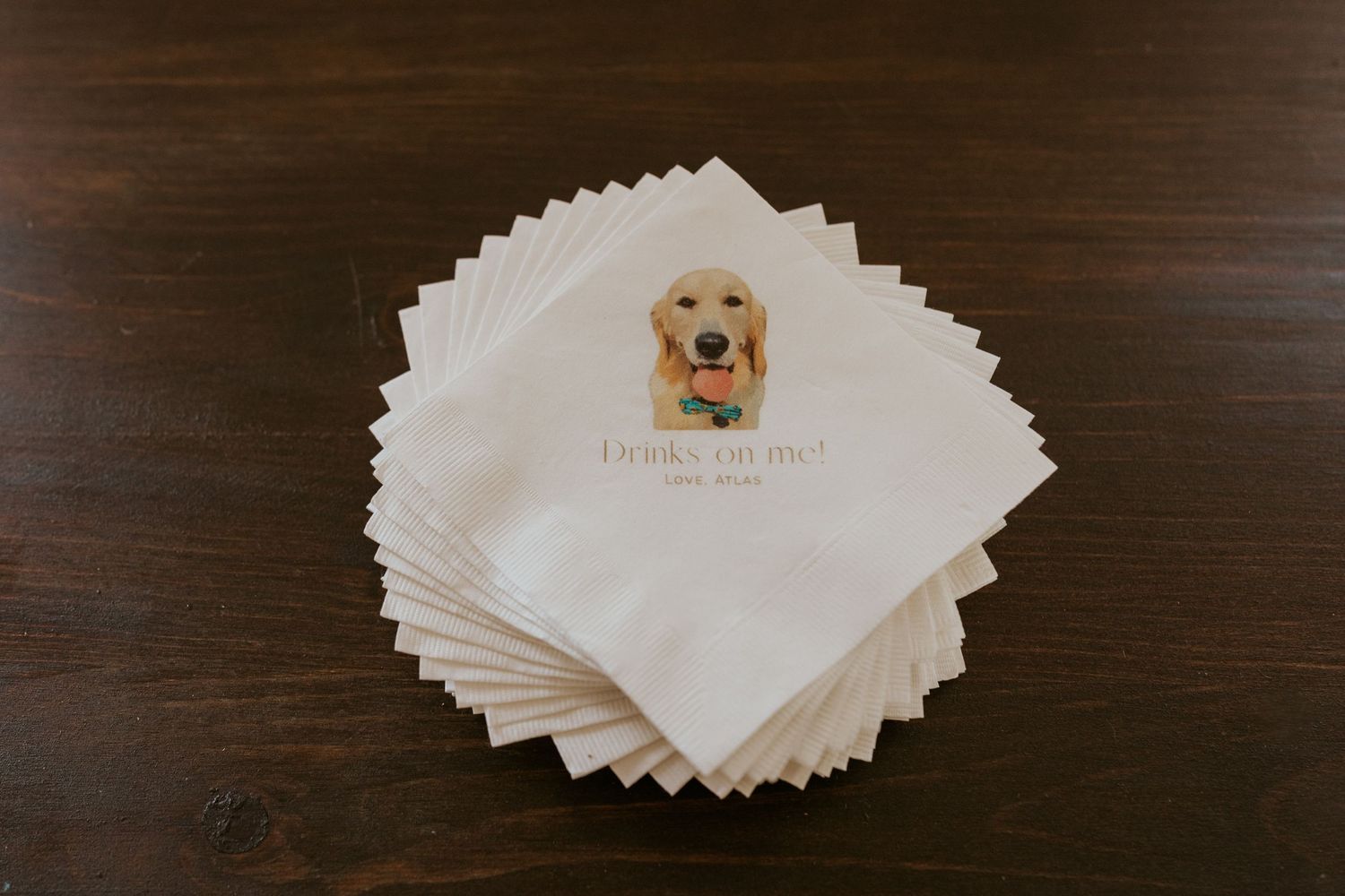 Custom wedding cocktail napkins featuring a golden retriever illustration stacked on wooden table.