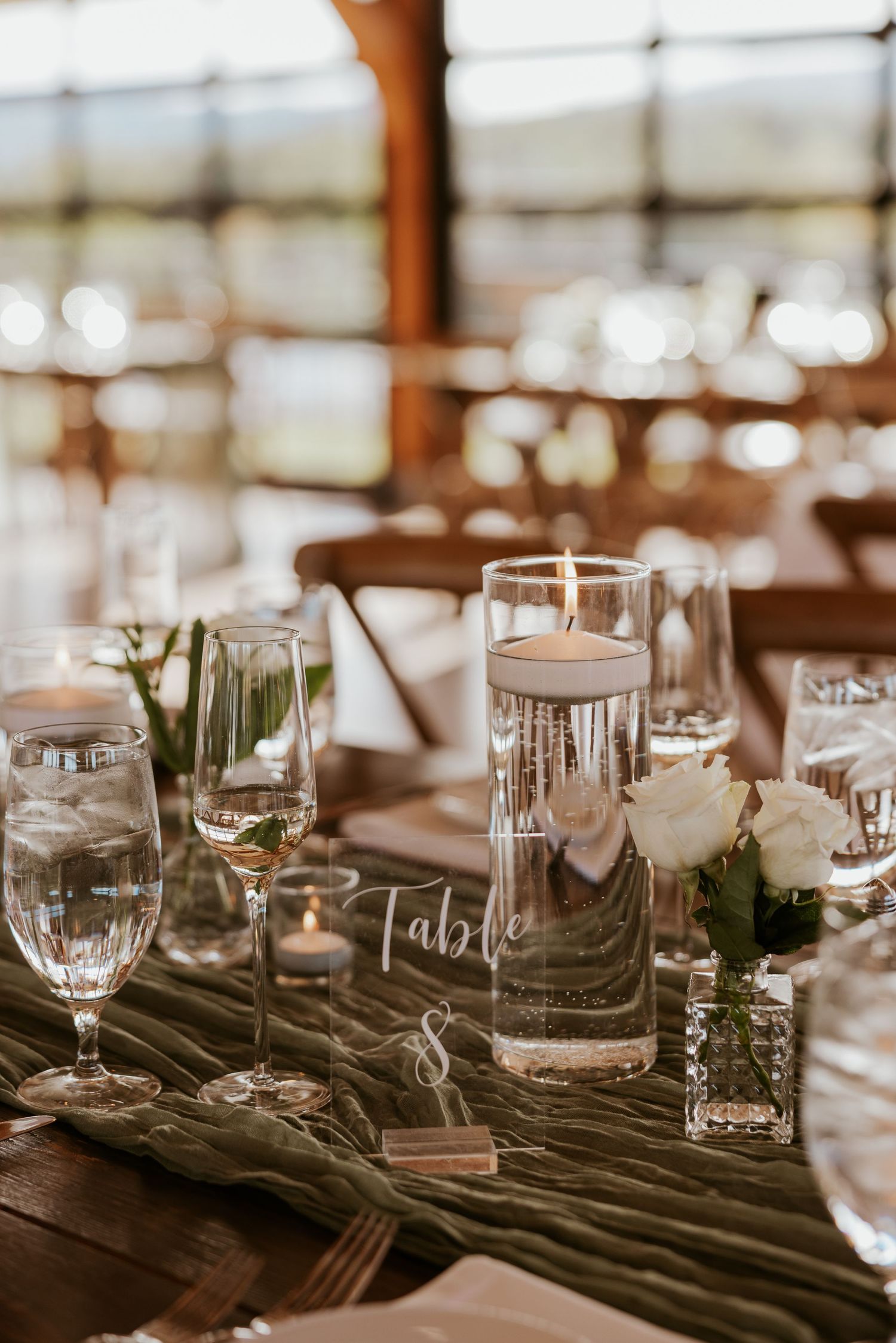 Elegant wedding reception table with floating candles, white roses, and velvet green table runner.