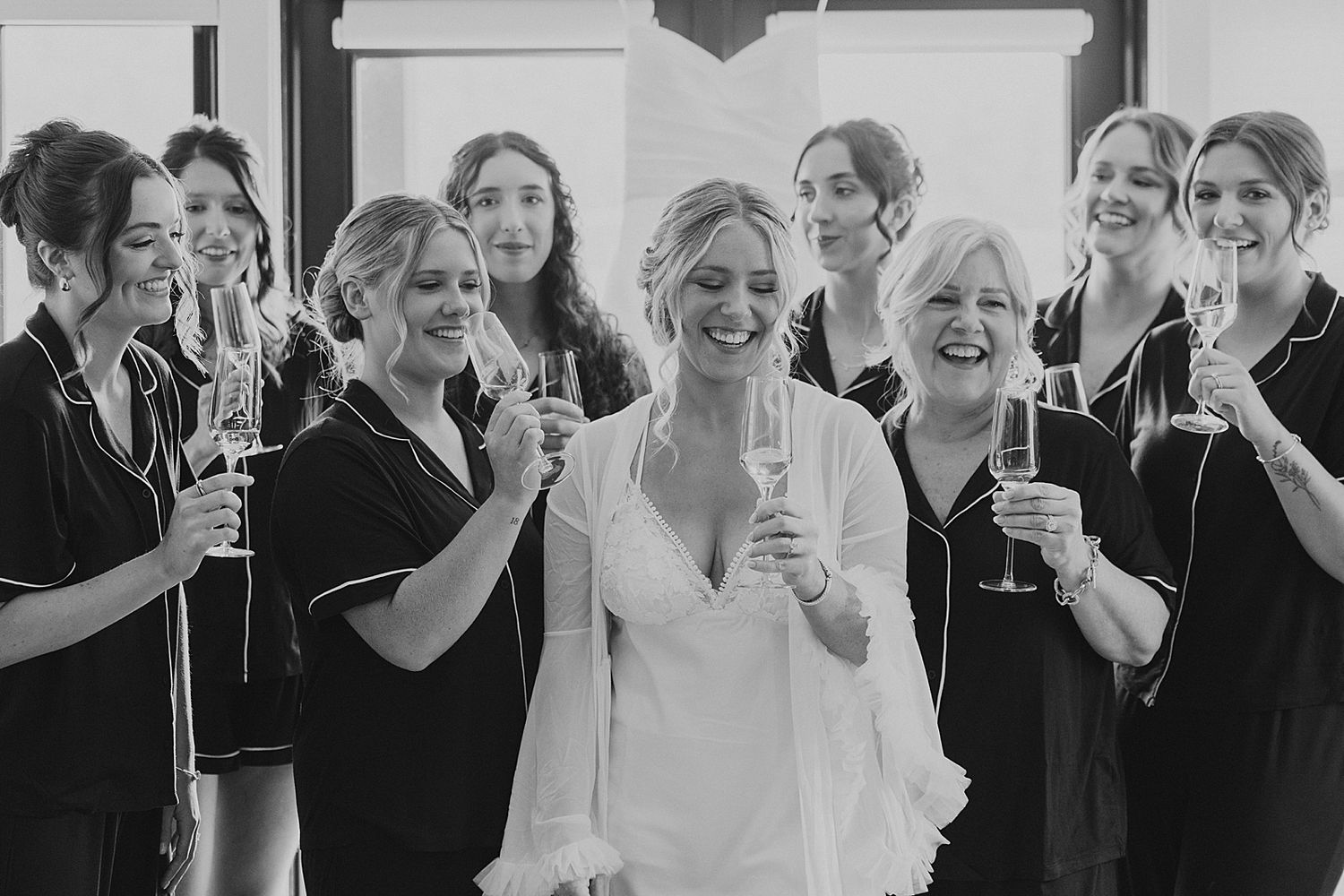 Bride in white robe having champagne with bridesmaids in black pajamas before her New Hampshire wedding