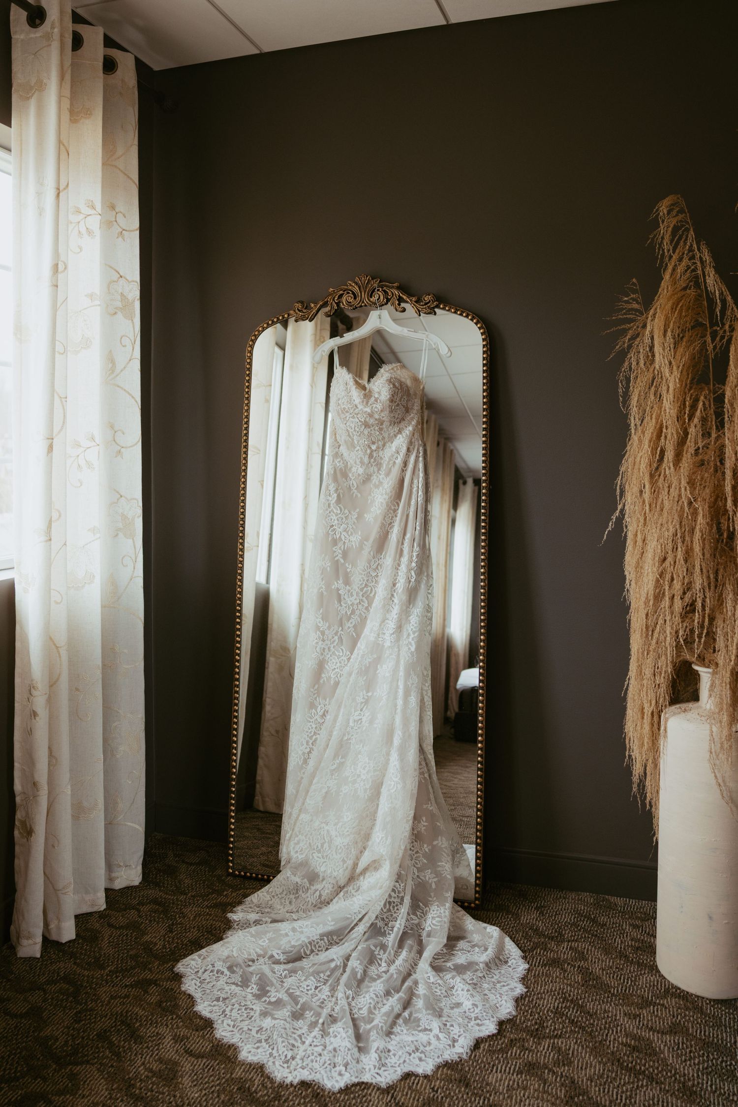 Four artistic photos of a vintage-style lace wedding dress with long train displayed against dark walls and white curtains.