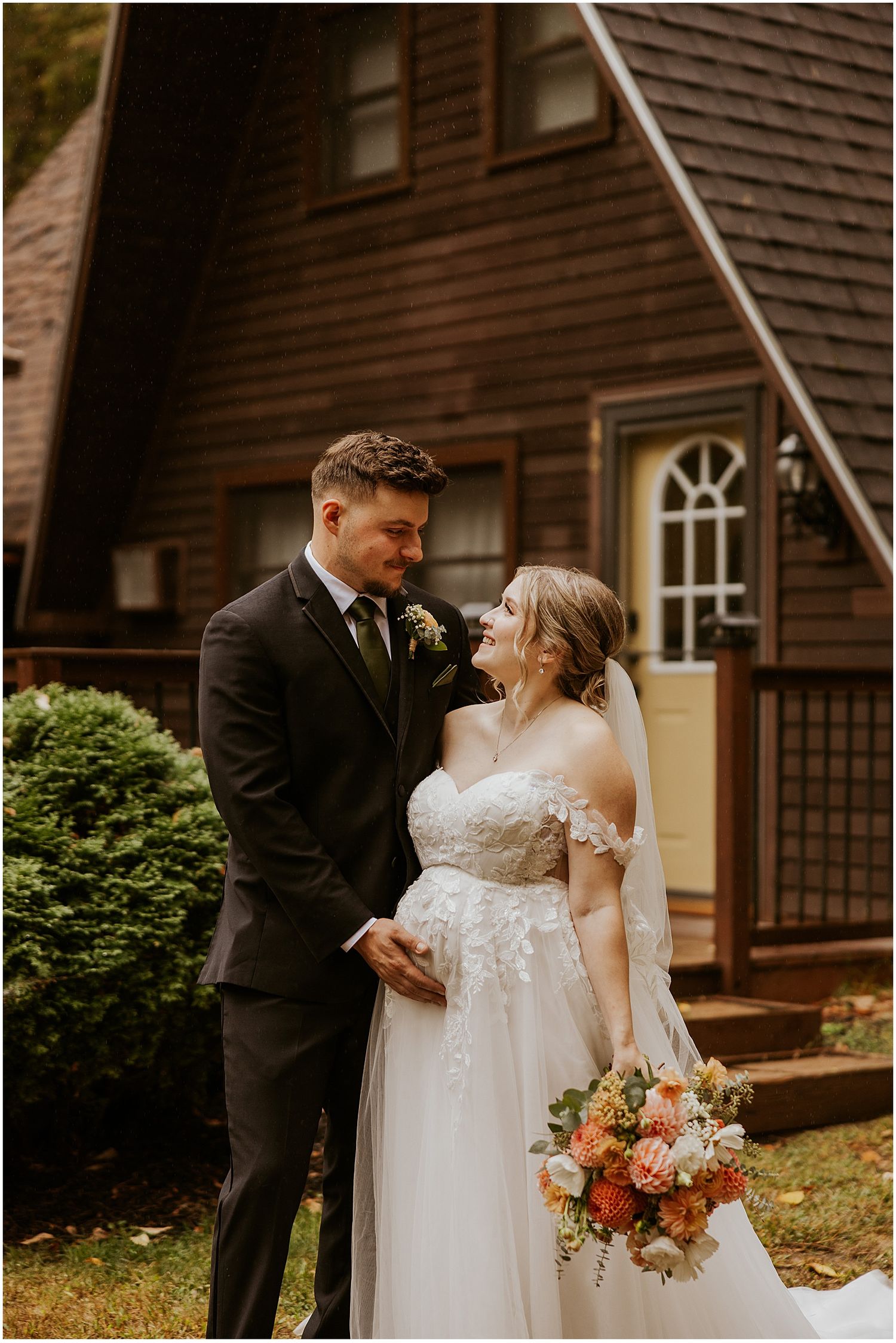 Intimate wedding portrait outside rustic brown cedar house with autumn bouquet.