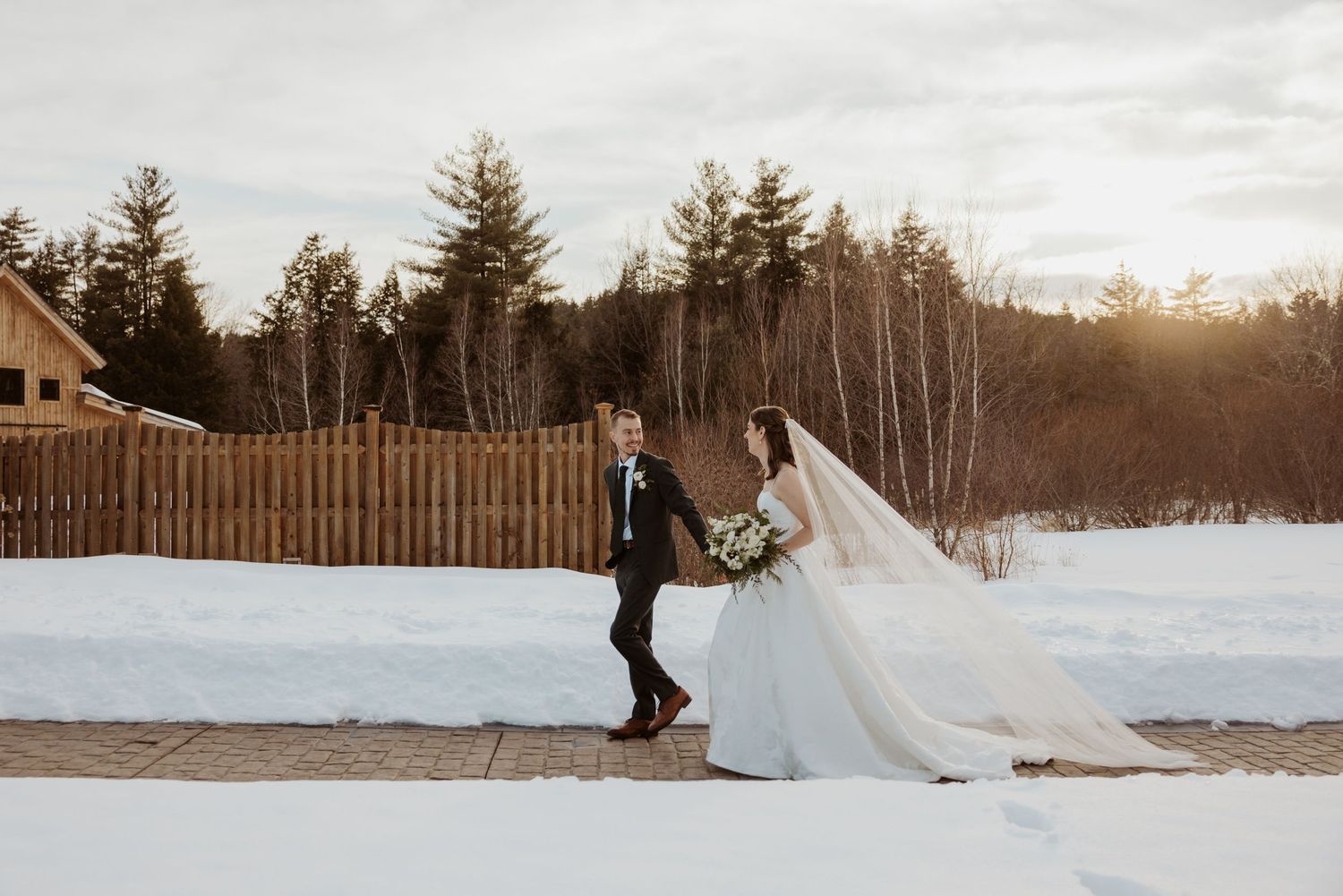 A snowy winter wedding photoshoot with evergreen trees and dramatic sunset lighting in the background.