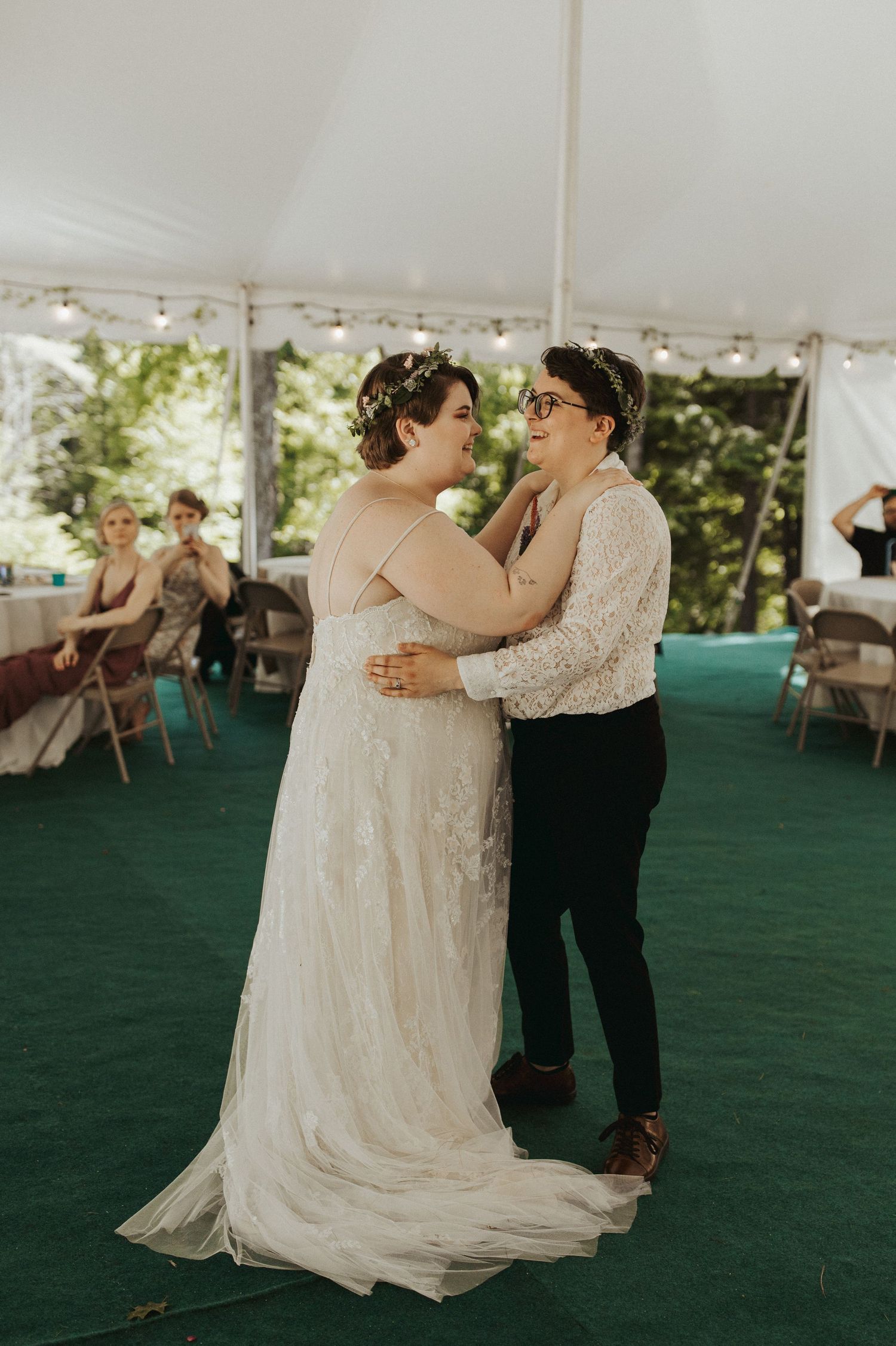 A couple dances together under a white tent with green carpeting at an outdoor wedding reception.