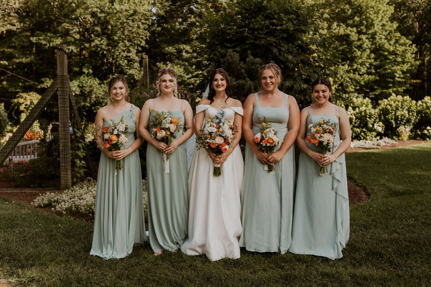Wedding party posed in a line on grass wearing light blue dresses and formal attire.