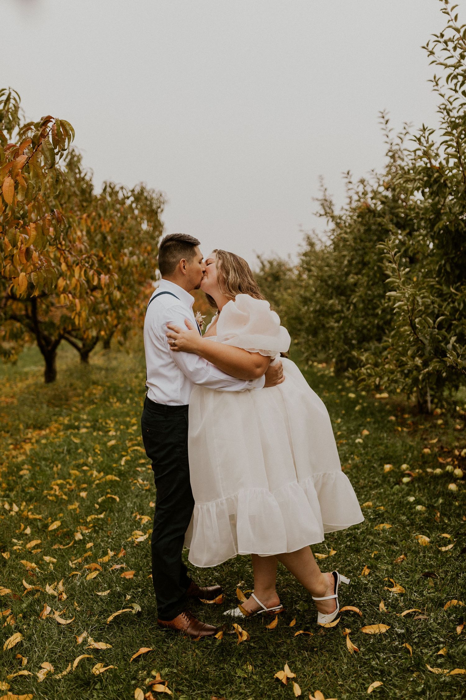 Terise and Jose kissing in between the rows of apple trees at Carter Hill Orchard in Concord New Hampshire]