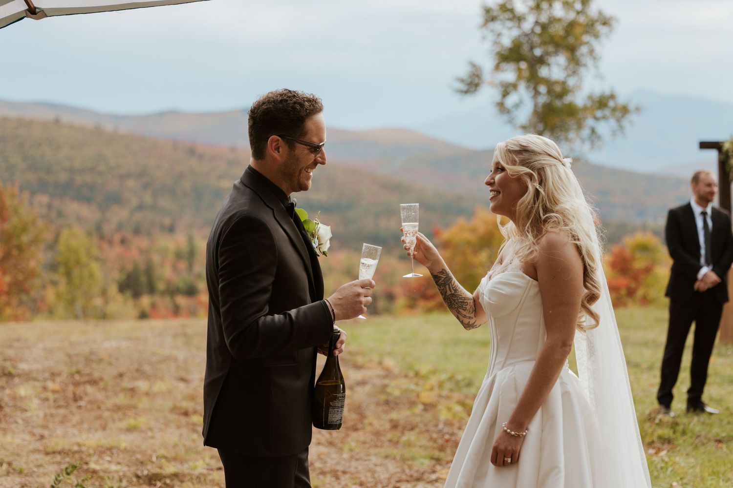 Bride and groom toast with champagne at an outdoor fall wedding with colorful mountain backdrop.