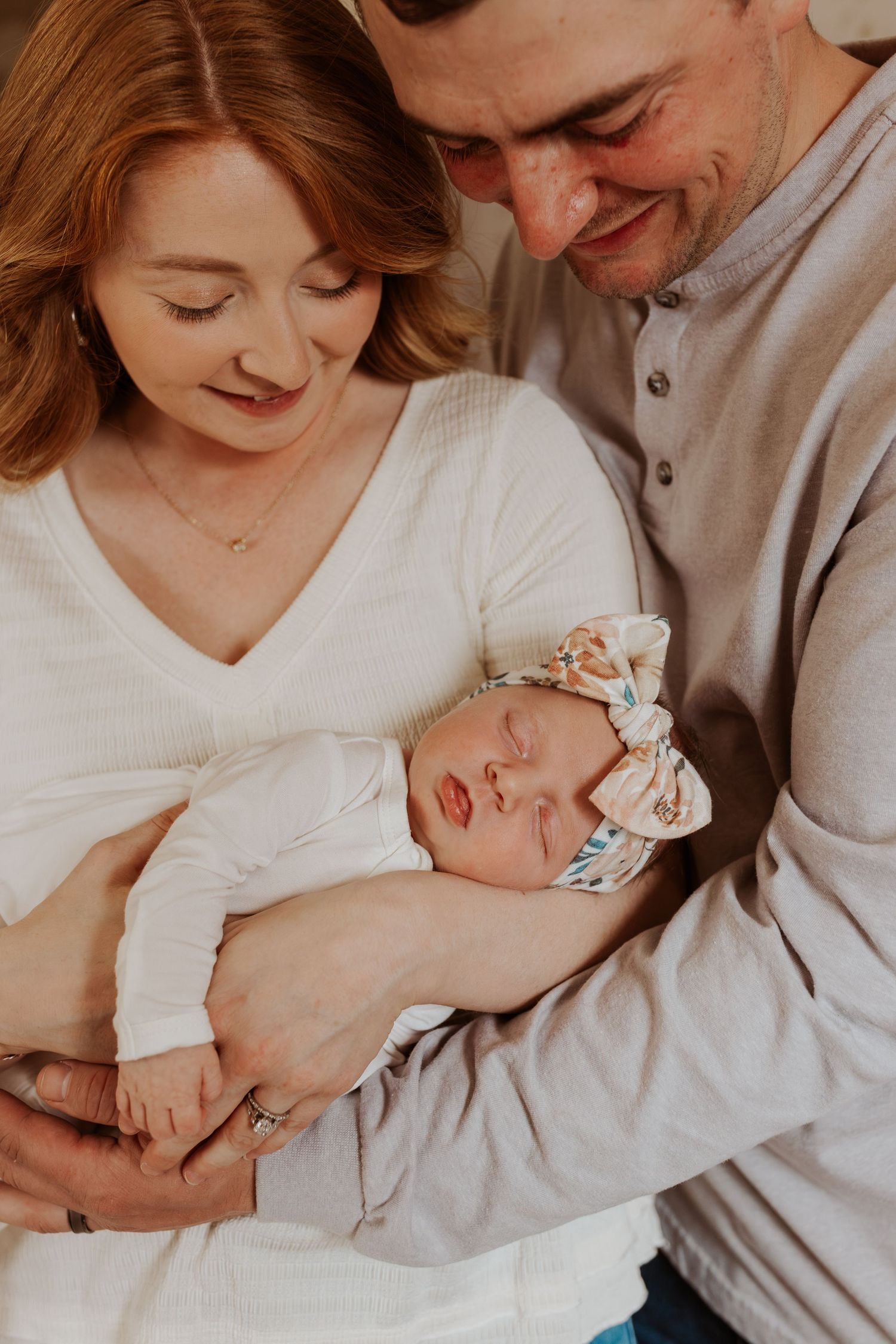 New parents lovingly cradle their sleeping newborn baby girl wearing a floral headband.