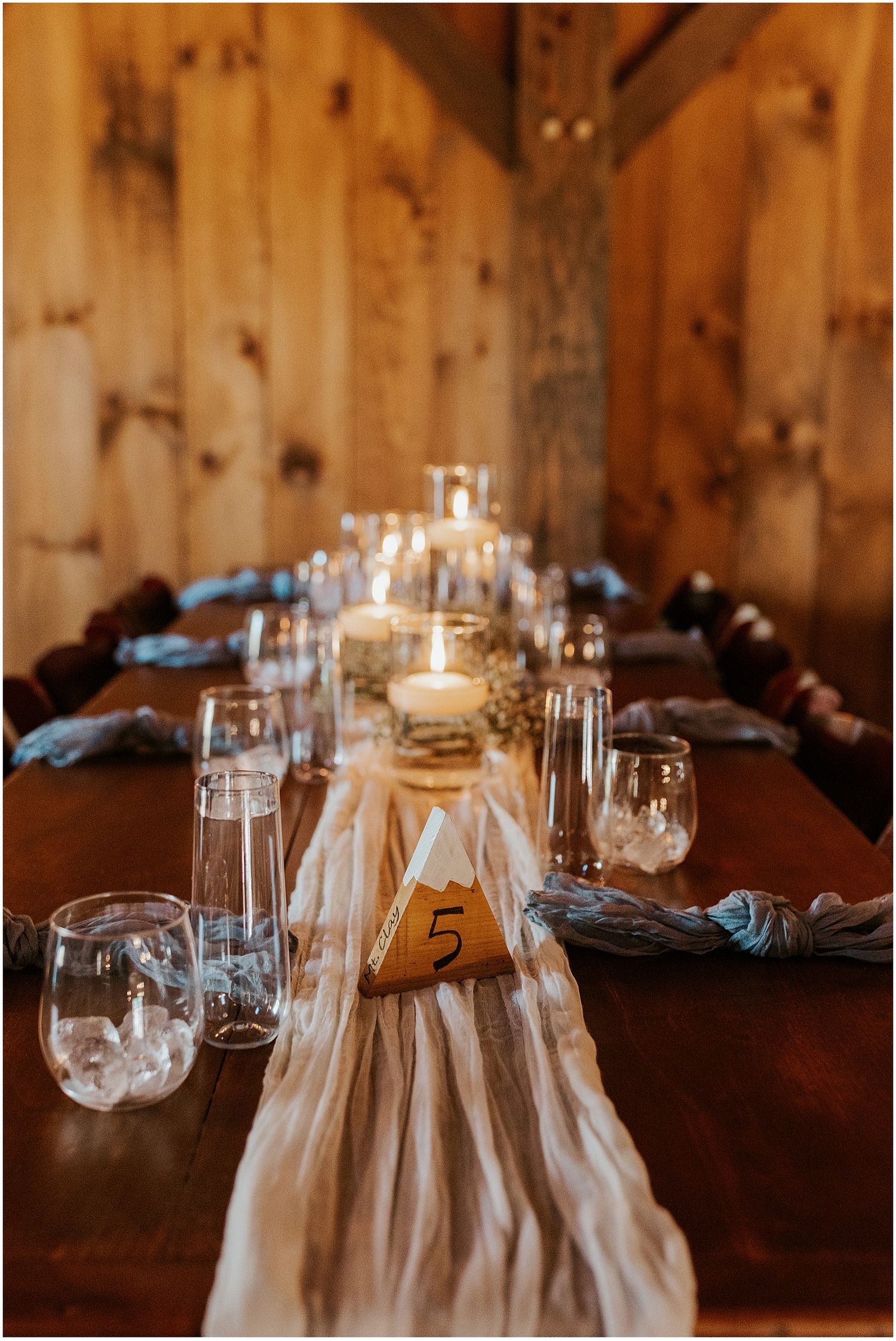 Wedding reception table settings with glassware and candles in a rustic wooden venue.