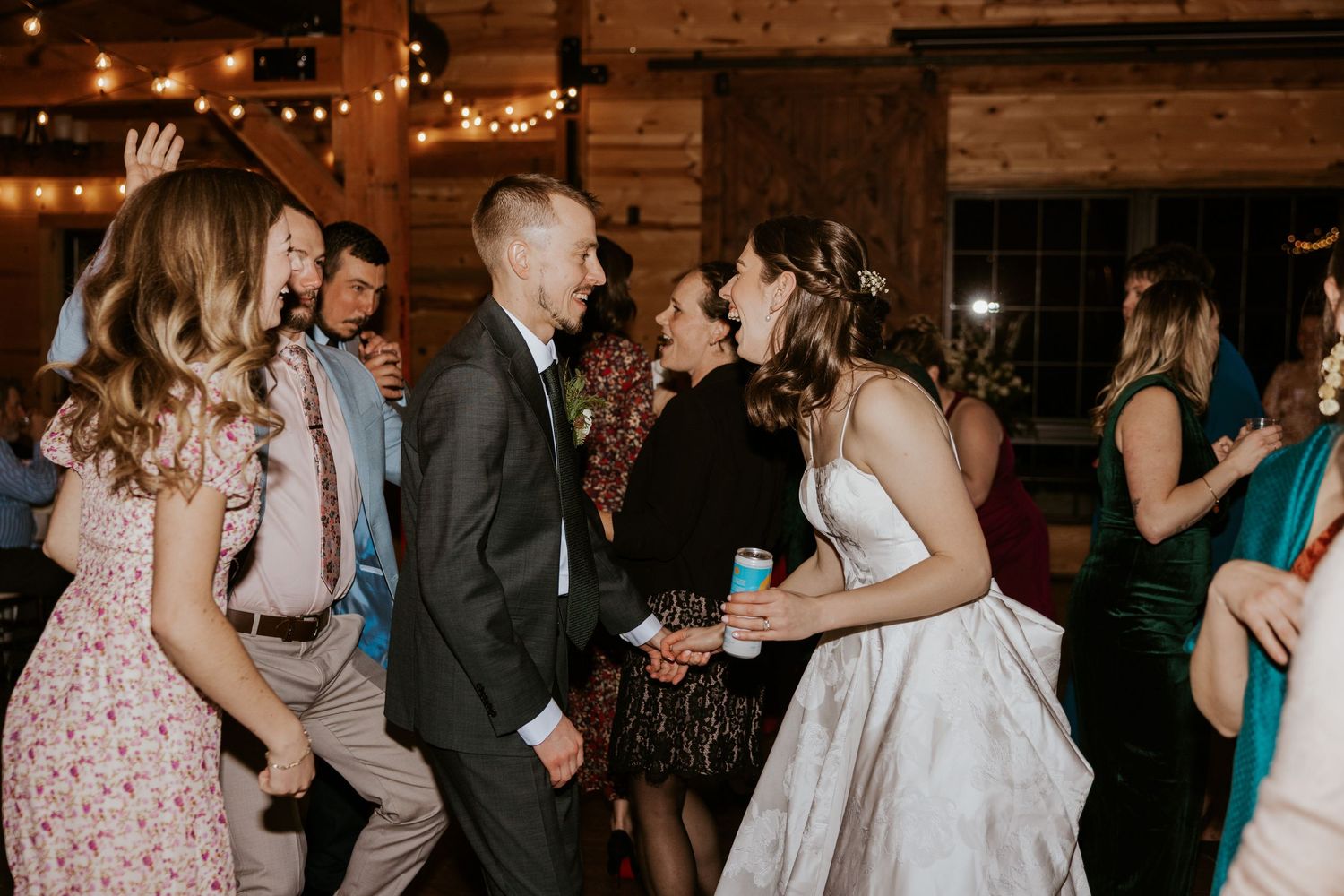 Wedding guests dancing together at an indoor reception with warm lighting and wooden walls.