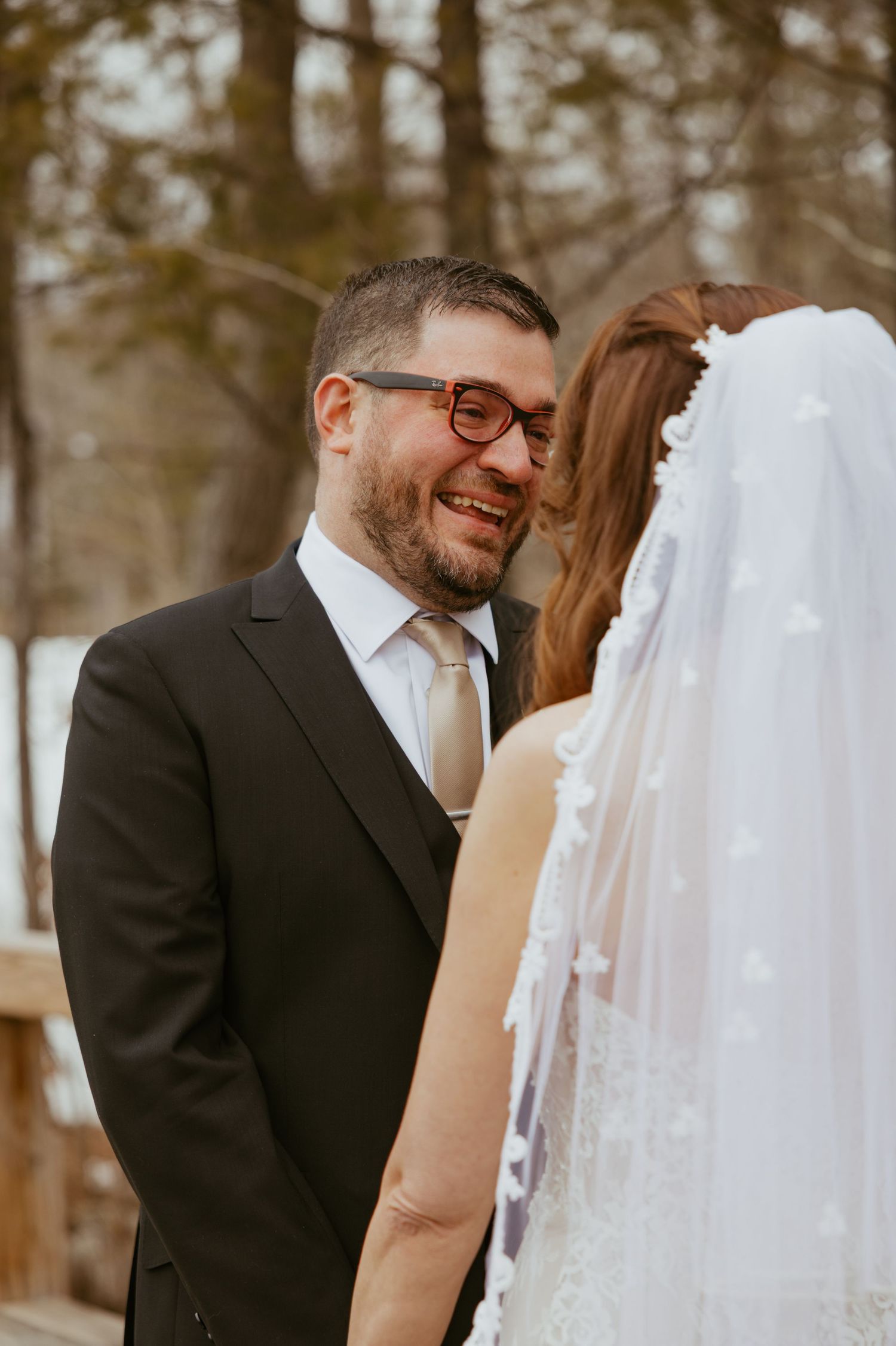 A romantic wedding moment captured in a wooded outdoor setting with warm natural lighting.