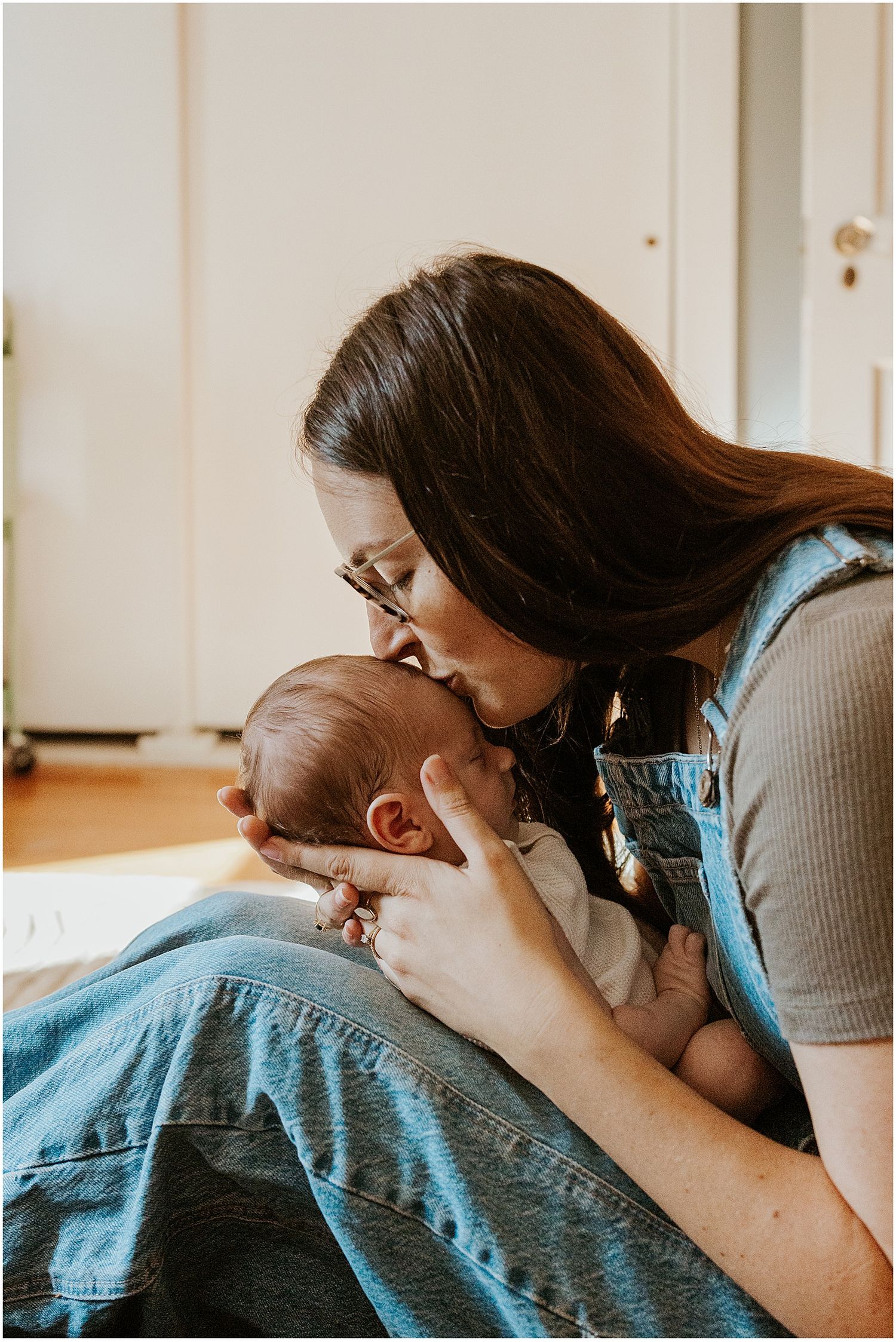 New Hampshire mom kissing her newborn baby's head while taking family photos at home