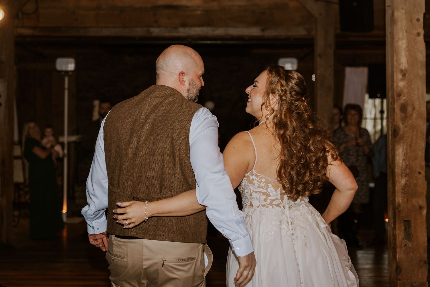 Couple dancing in rustic barn venue with string lights and wooden beams.