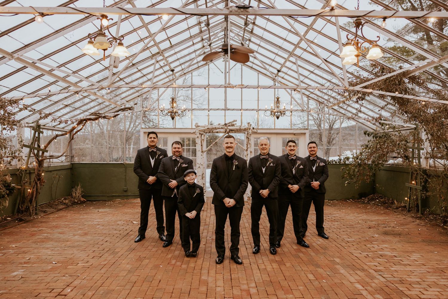 Groom and groomsmen in black suits posing inside a stunning glass greenhouse venue.