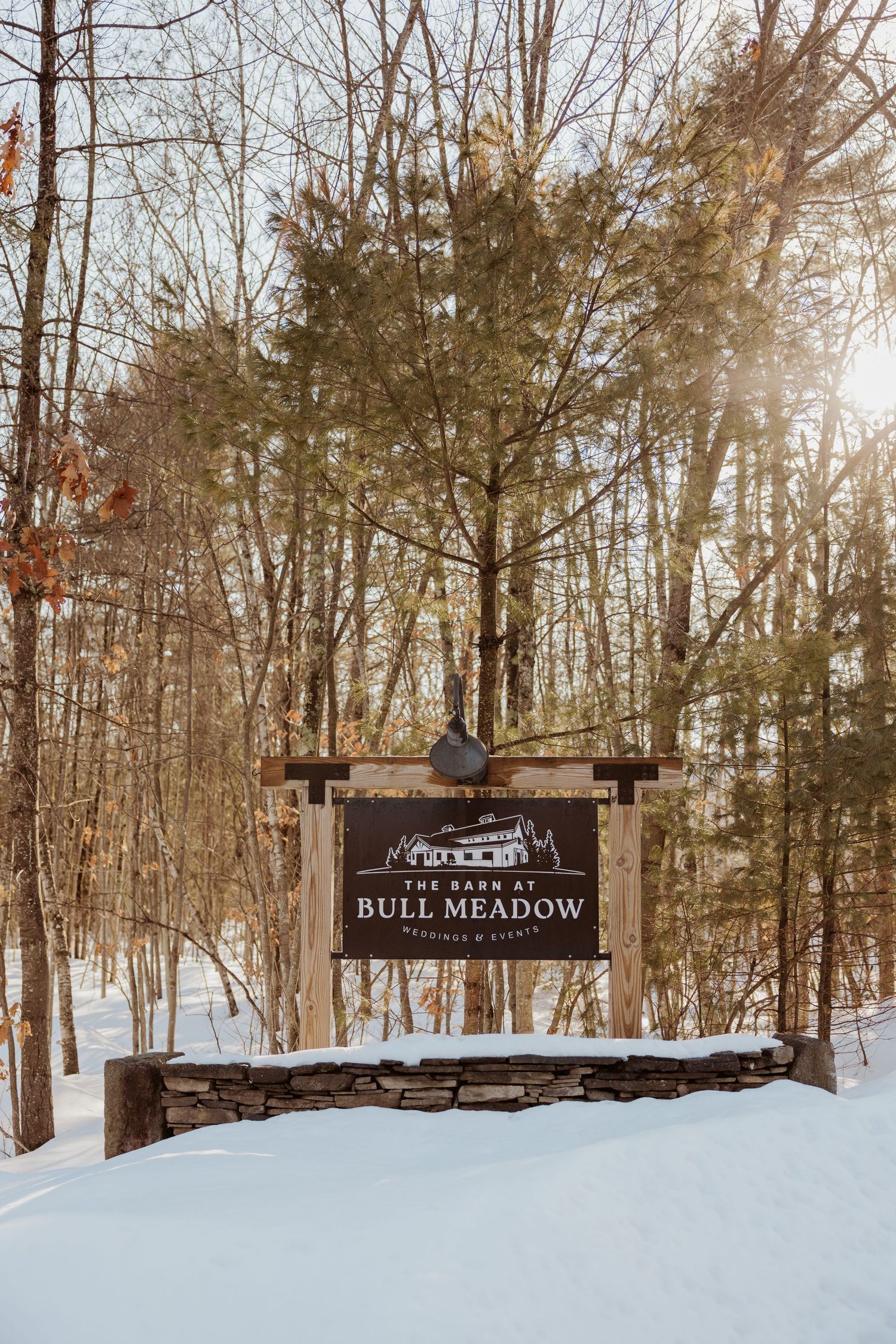 Rustic wooden sign for Bull Meadow park entrance covered in snow with bare winter trees in the background.