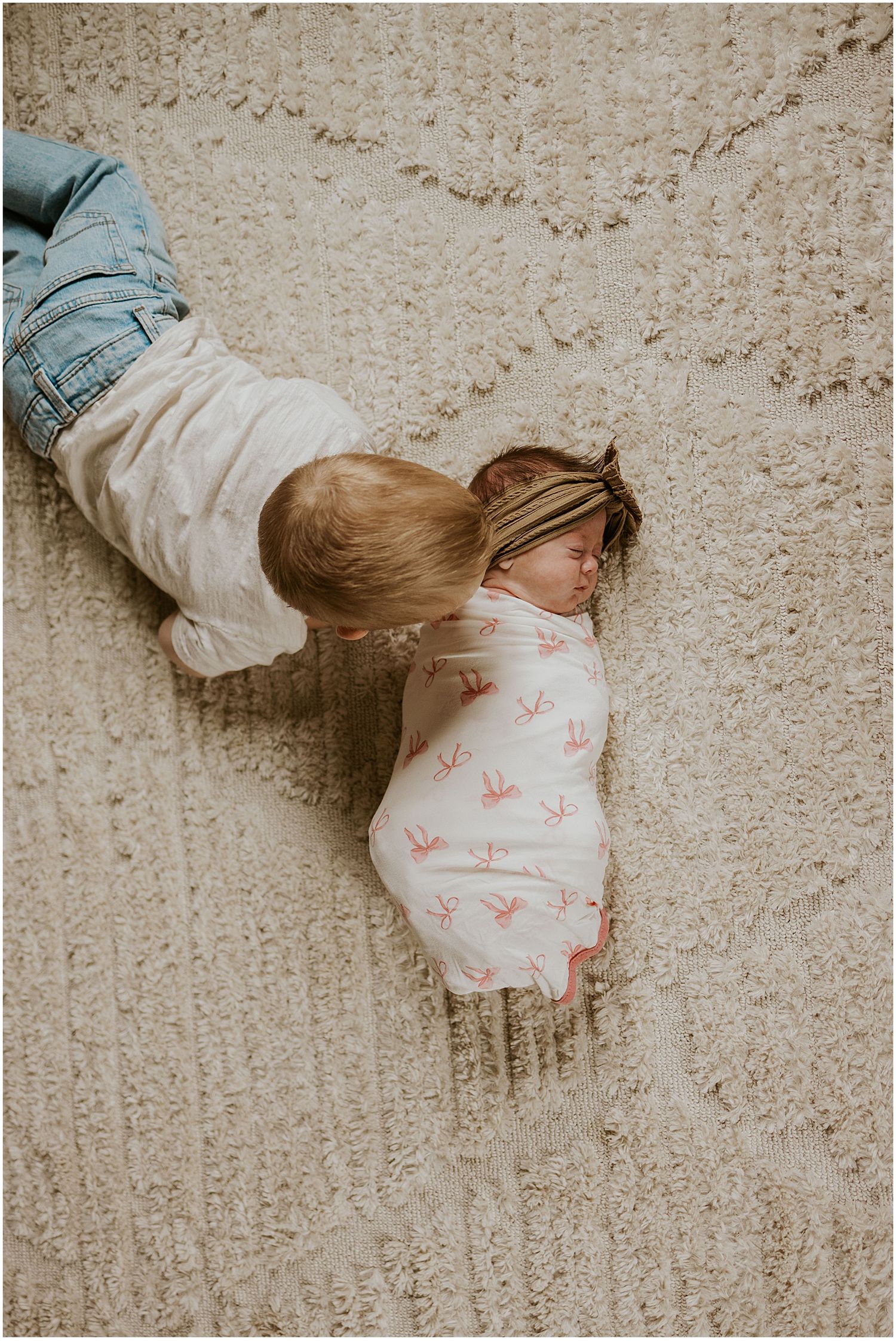 Toddler playing with his newborn baby sister on the floor