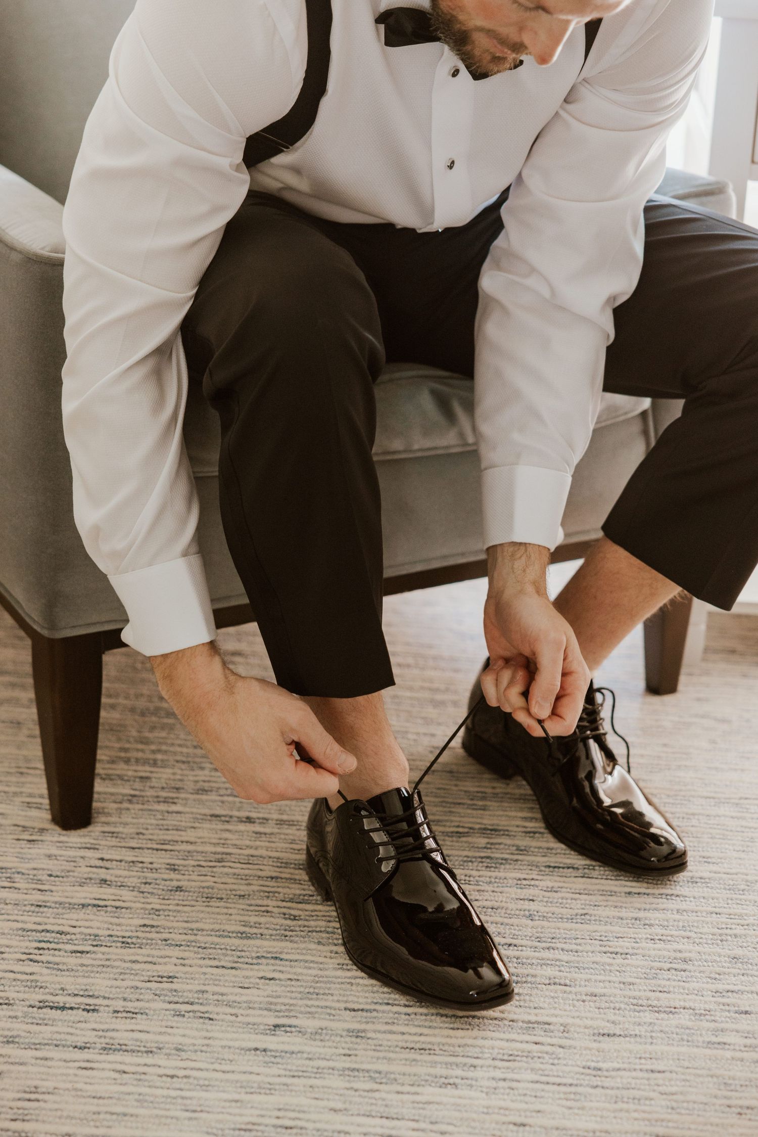 A sequence of hands tying formal black dress shoes on a light carpet, showing the step-by-step lacing process.