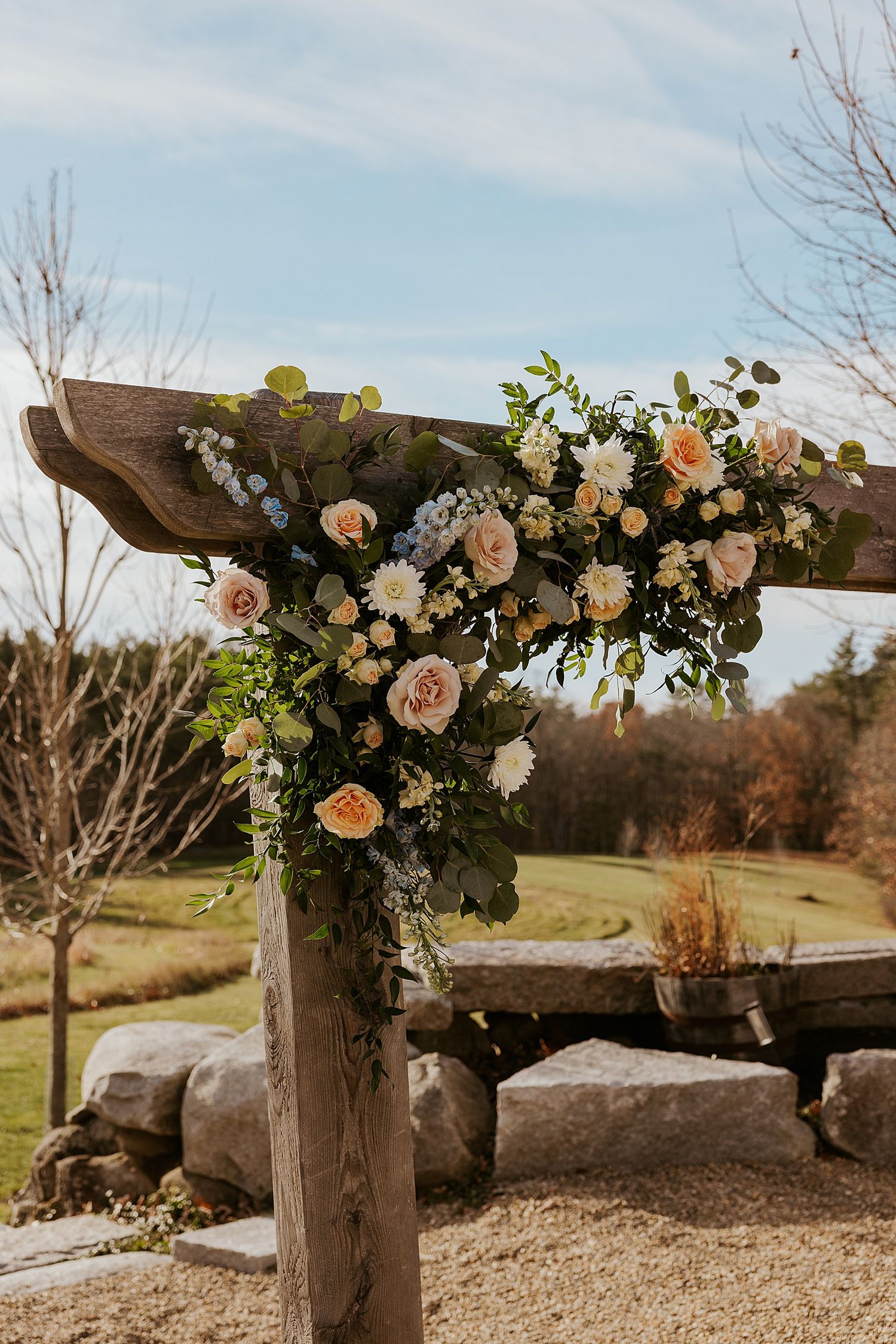 A rustic wooden wedding arch covered in orange, peach and cream florals for a New Hampshire barn wedding