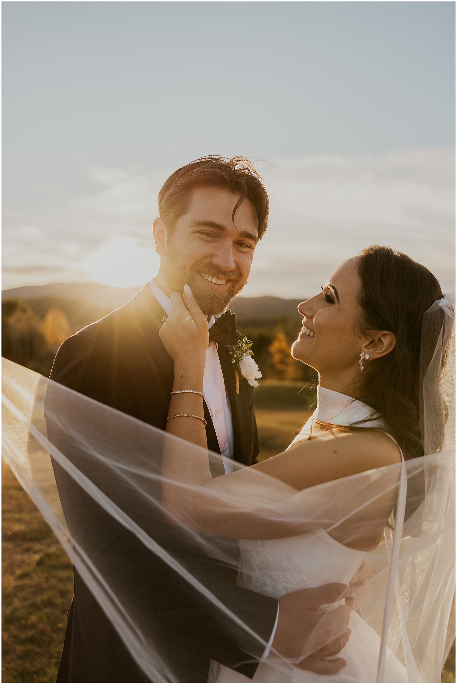 Intimate wedding portrait with flowing veil backlit by golden sunset light.