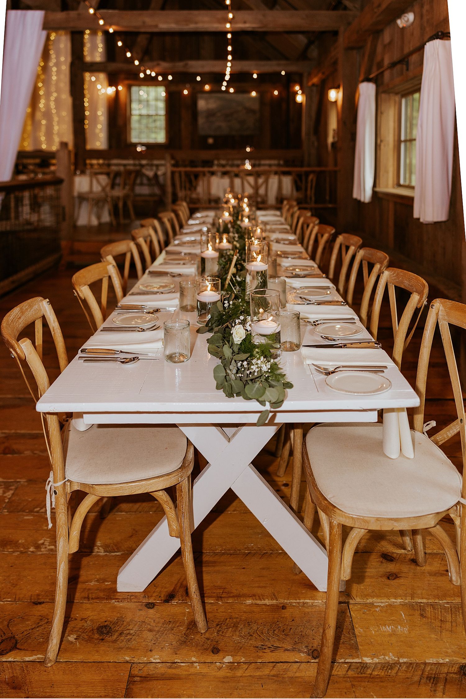 Elegant farmhouse wedding reception tables with white linens and simple greenery centerpieces.