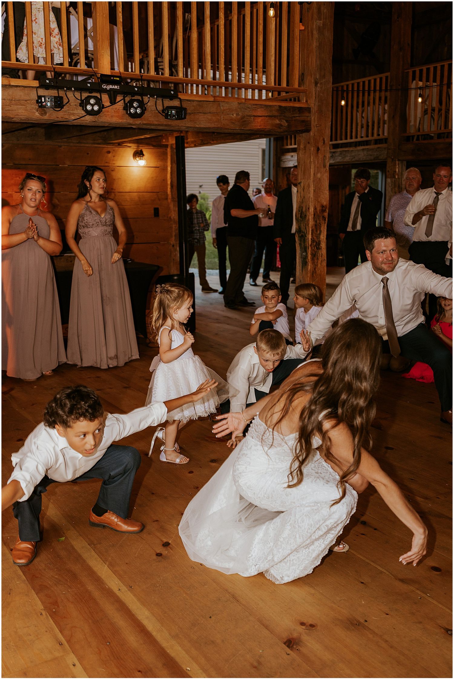 Wedding guests dancing and having fun on a wooden dance floor in a rustic barn setting.