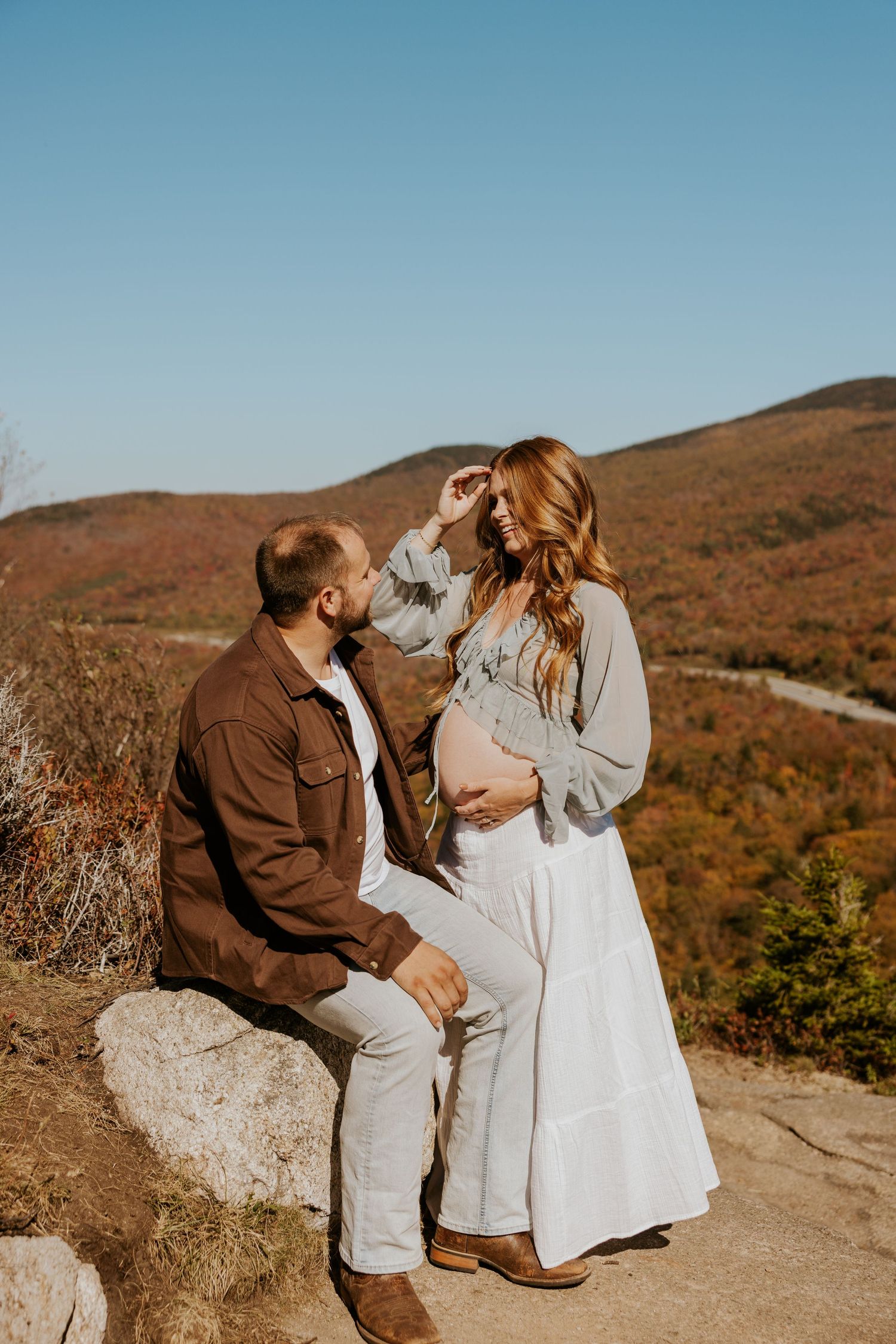 Couple sharing tender moment on mountain overlook with stunning autumn valley landscape behind them.