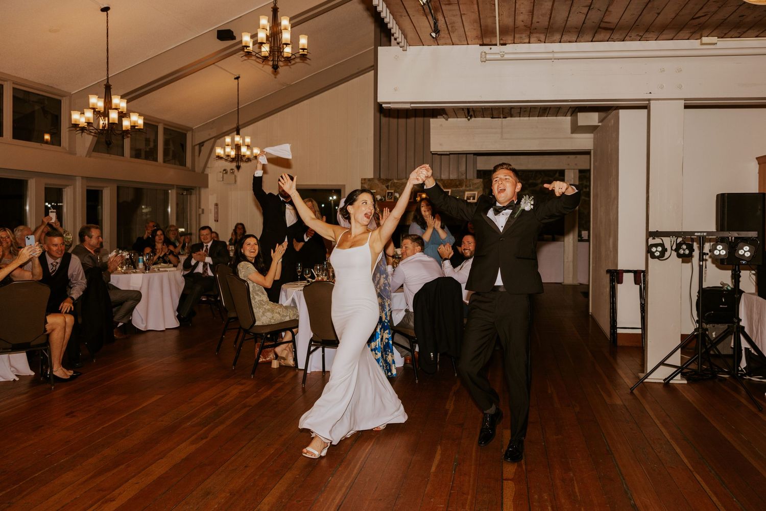 Bride and groom make grand entrance with raised arms into wedding reception hall.