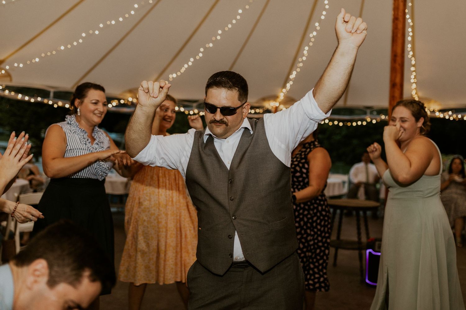 Wedding reception dance floor filled with guests celebrating under warm string lights.