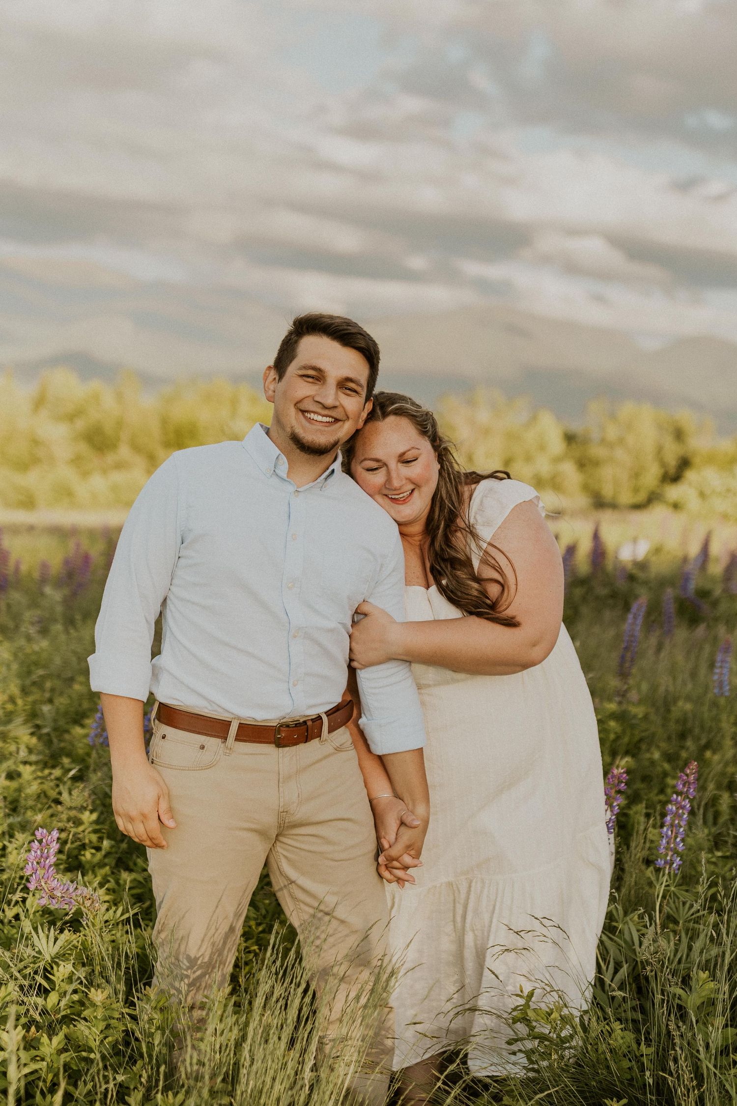 Terise hugging onto Jose's arm and smiling during an engagement photoshoot in the lupine fields of Sugar Hill NH.