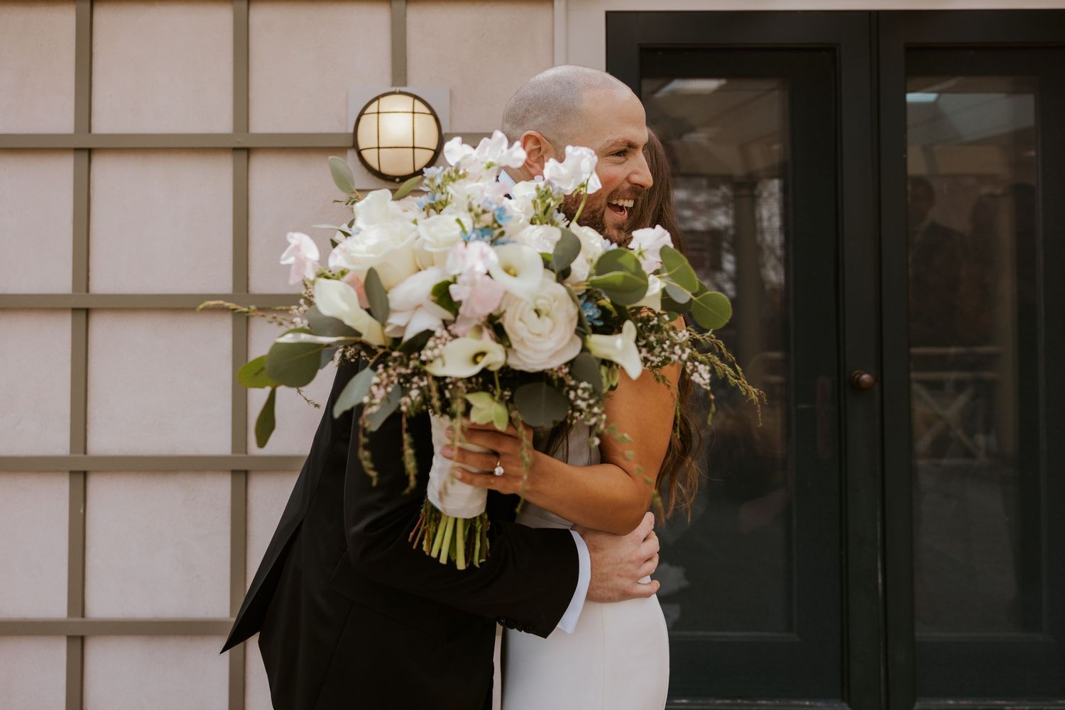 A bride and groom hold white floral bouquets while standing in front of a traditional Japanese shoji screen wall.