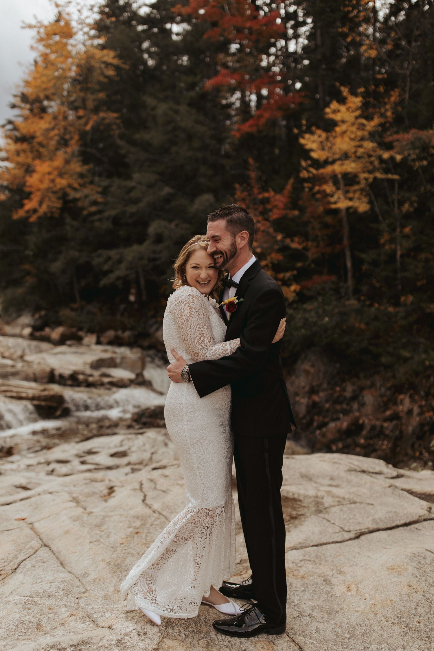 A couple shares an intimate moment on rocky terrain surrounded by autumn foliage.