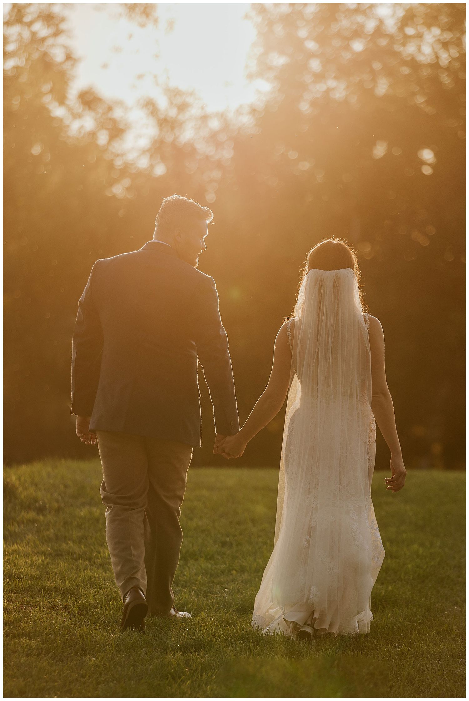 Silhouette of newlyweds walking hand in hand during golden hour sunset.