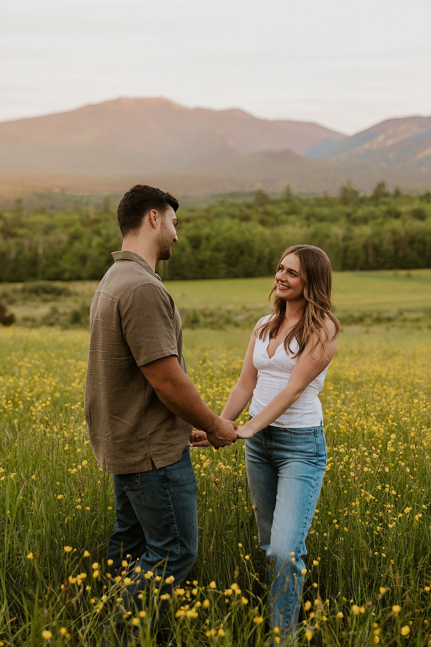Couple holding hands in a wildflower meadow with mountain sunset backdrop.