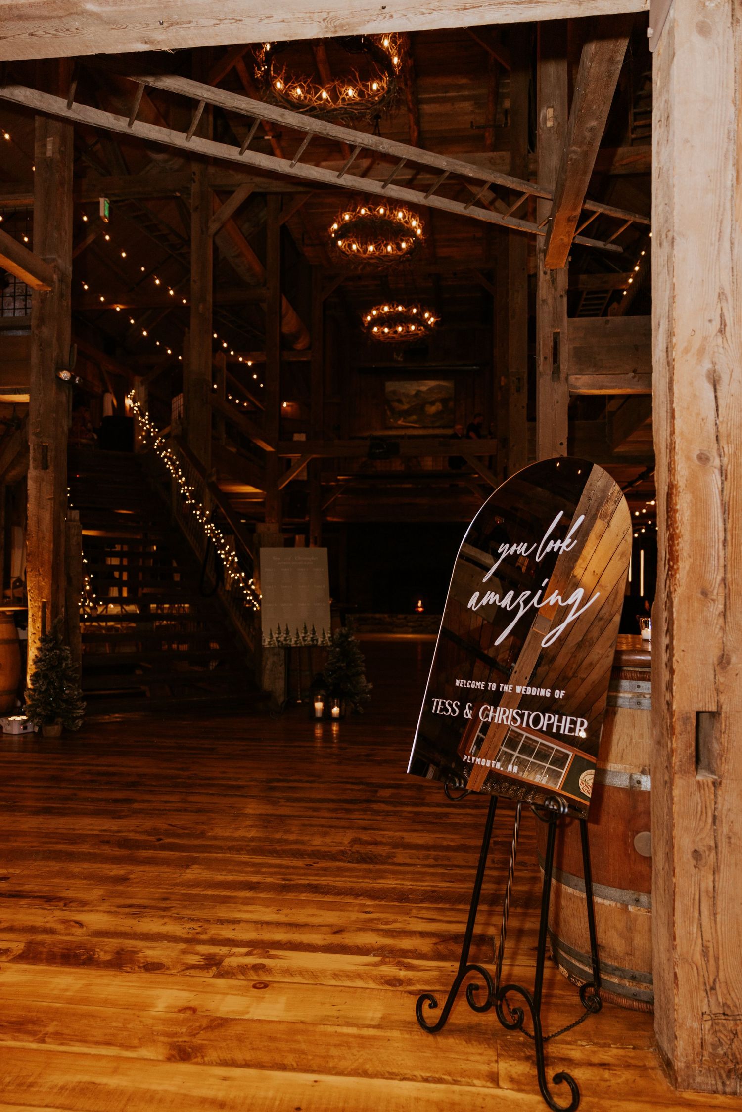 Rustic barn wedding venue with warm string lights, wood beams, and elegant welcome sign for Yess and Christopher's wedding.