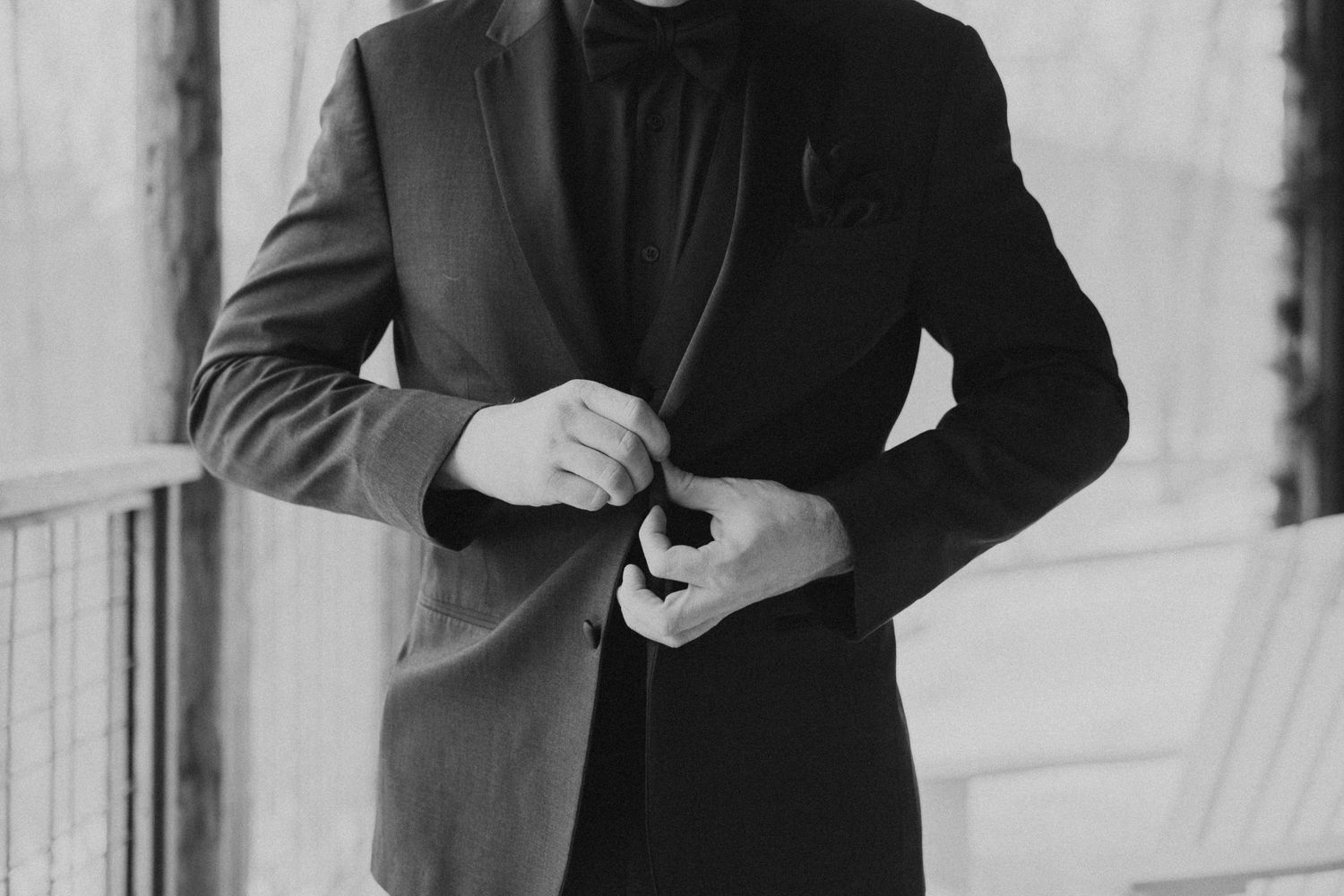 Black and white photo of a man in a dark suit buttoning his jacket, elegant formal attire.