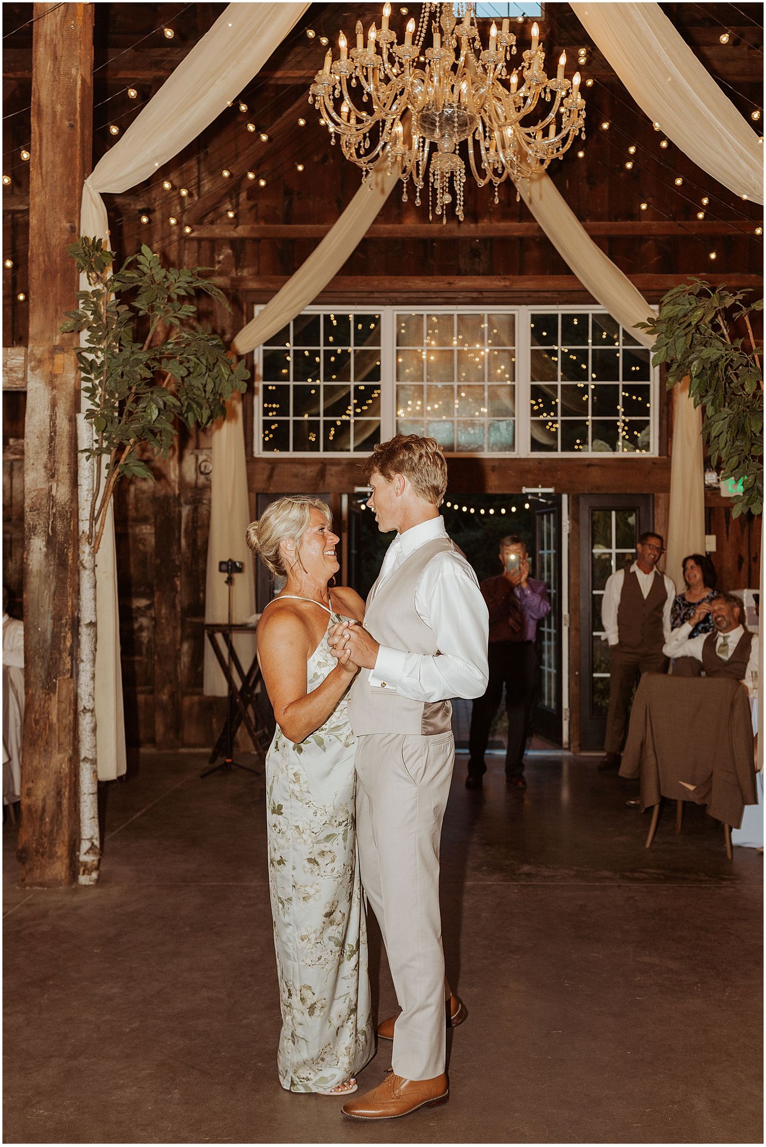 Couple dancing in an elegantly decorated barn venue with string lights and white draping.