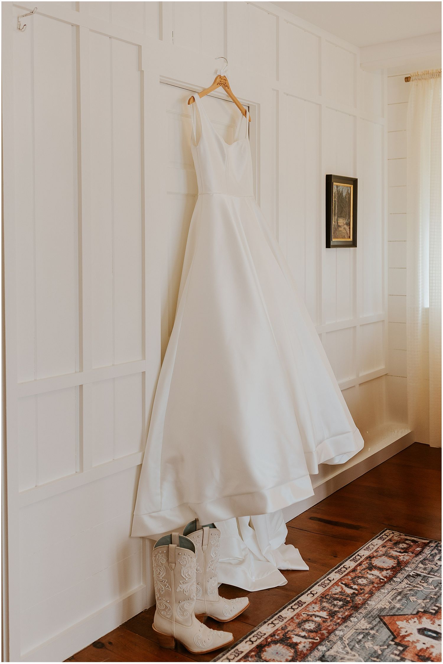 A white wedding dress and boots displayed against white paneled walls in natural light.