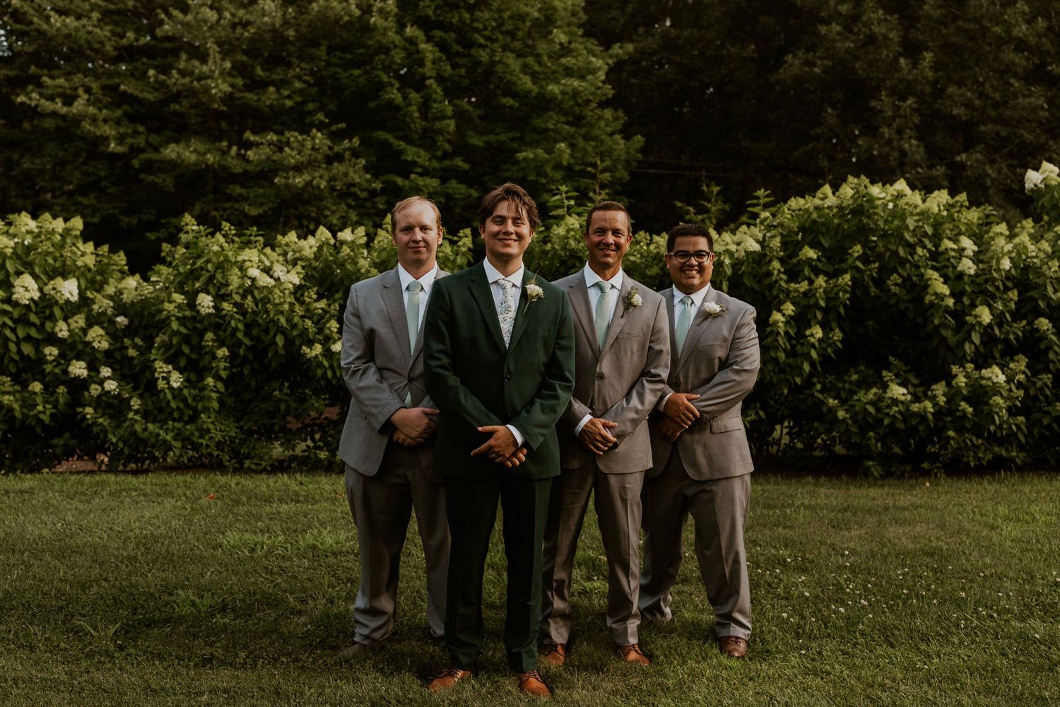 Wedding party members arranged on grass for formal group photos.