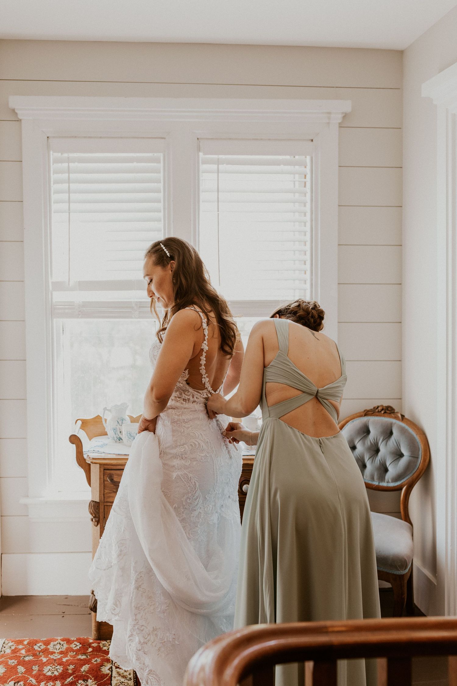 Wedding preparations in a bright white room with bridesmaids helping with final touches.