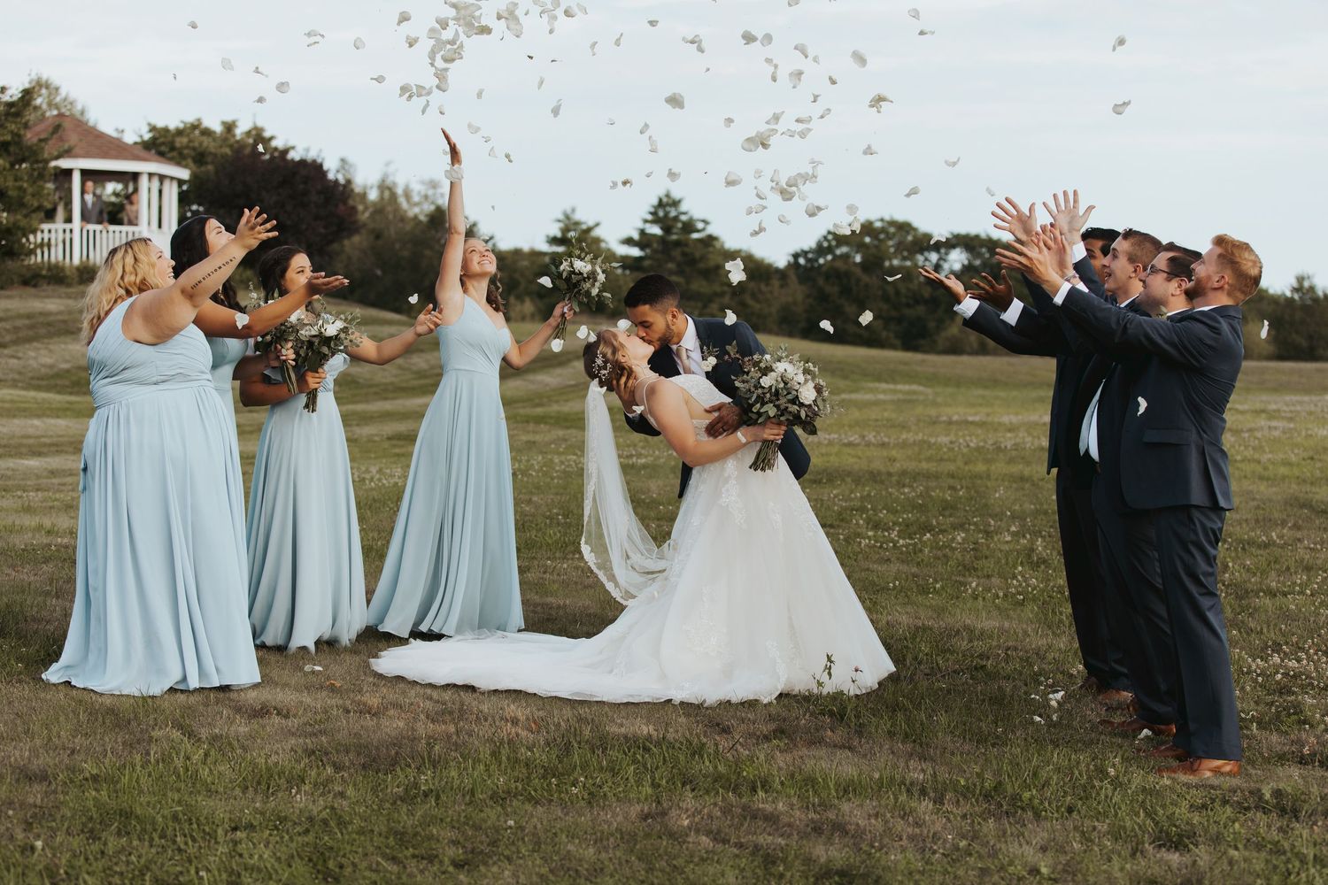 groom dipping his bride while the bridal party tosses rose petals into the air