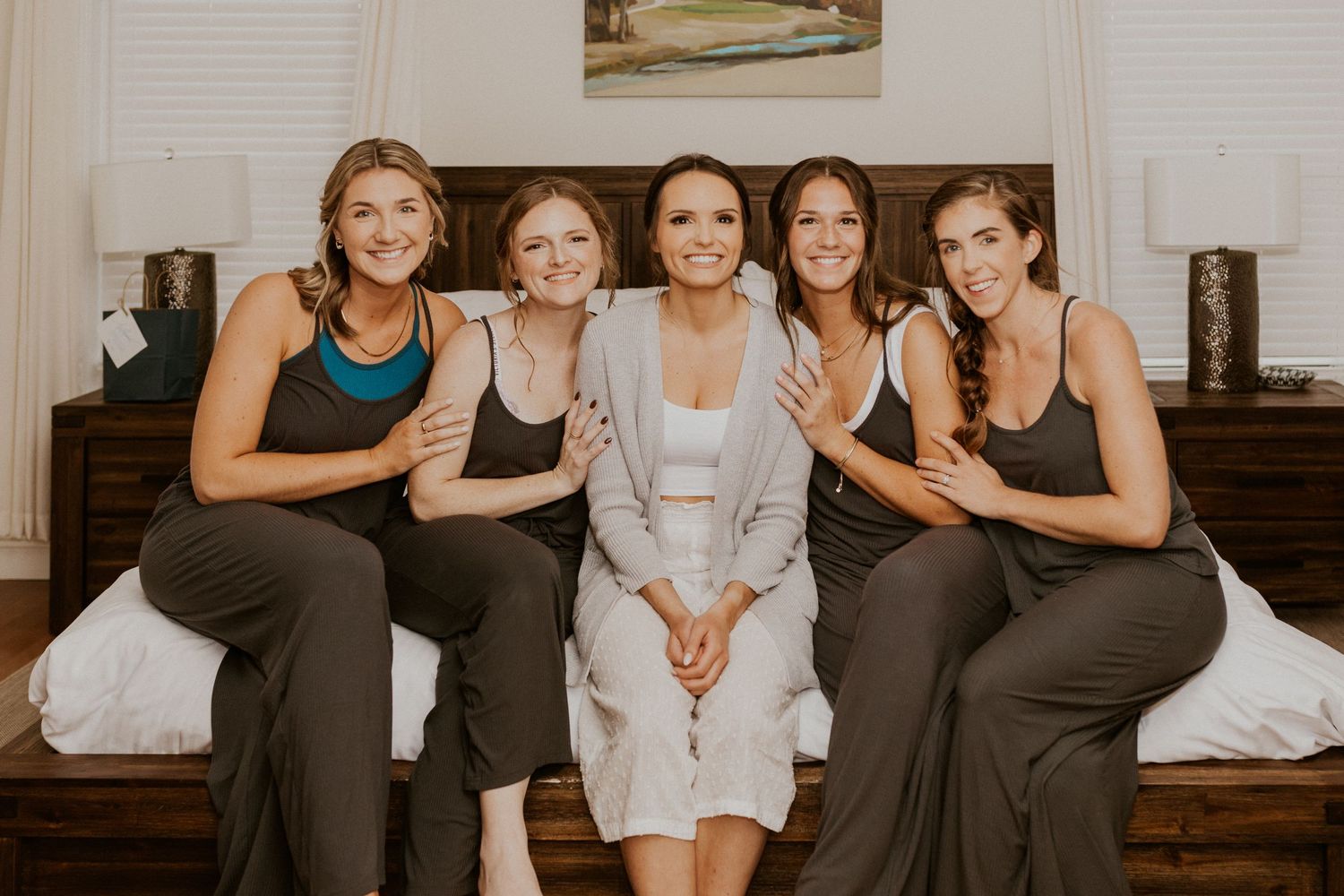 Abbie and her bridesmaids sitting together on the edge of the bed for a pajama photo before they all changed.