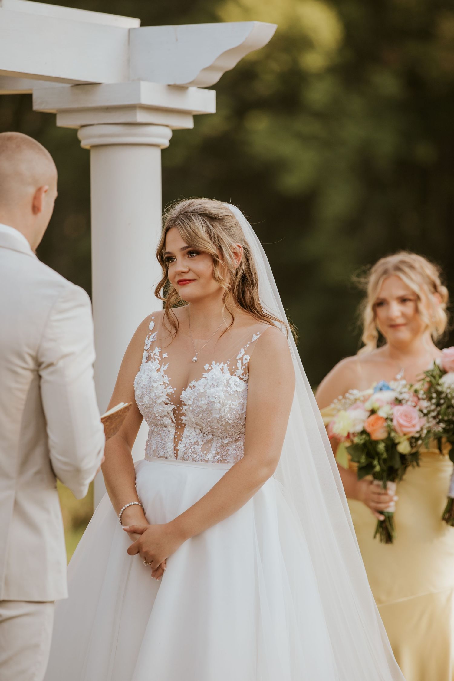 Bride in lace illusion bodice ball gown wedding dress with veil exchanging vows at outdoor garden ceremony.