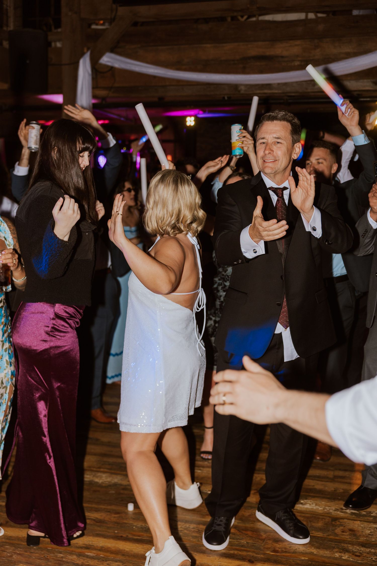 Wedding guests dance with glow sticks at lively rustic barn wedding reception.