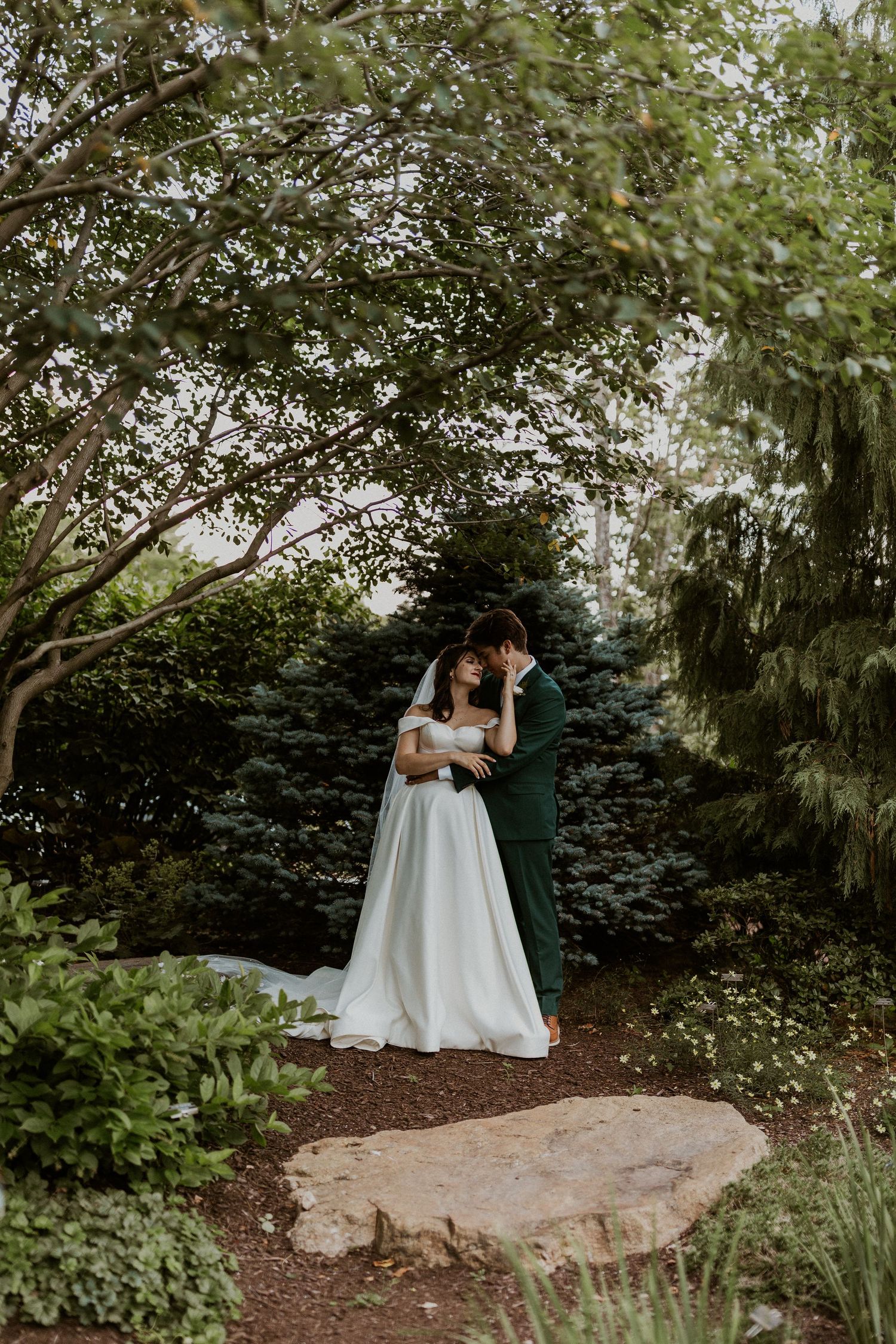 Couple shares romantic moment on large garden rock surrounded by greenery.