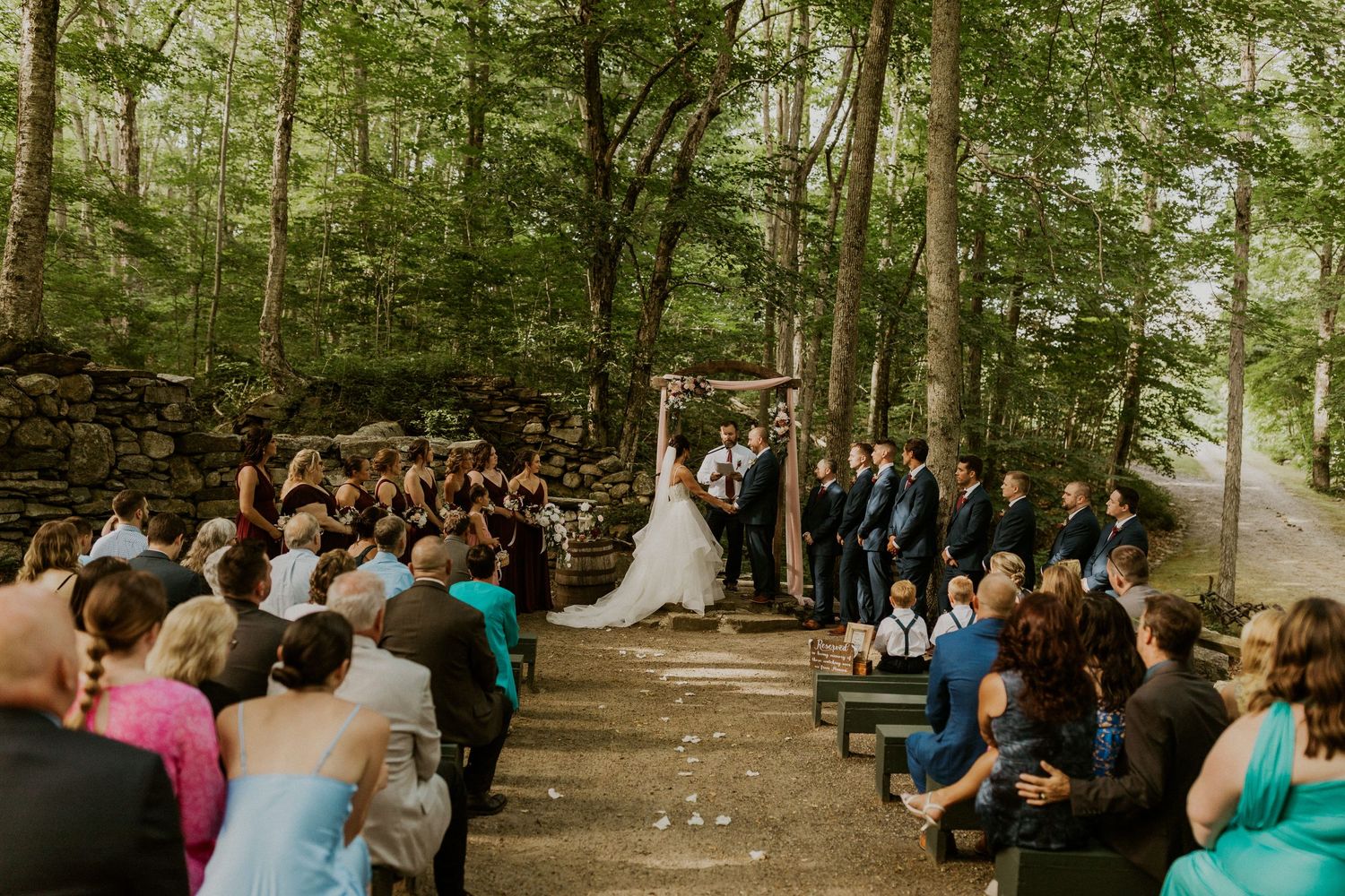 Wedding ceremony guests seated in rows outdoors in a wooded forest setting.