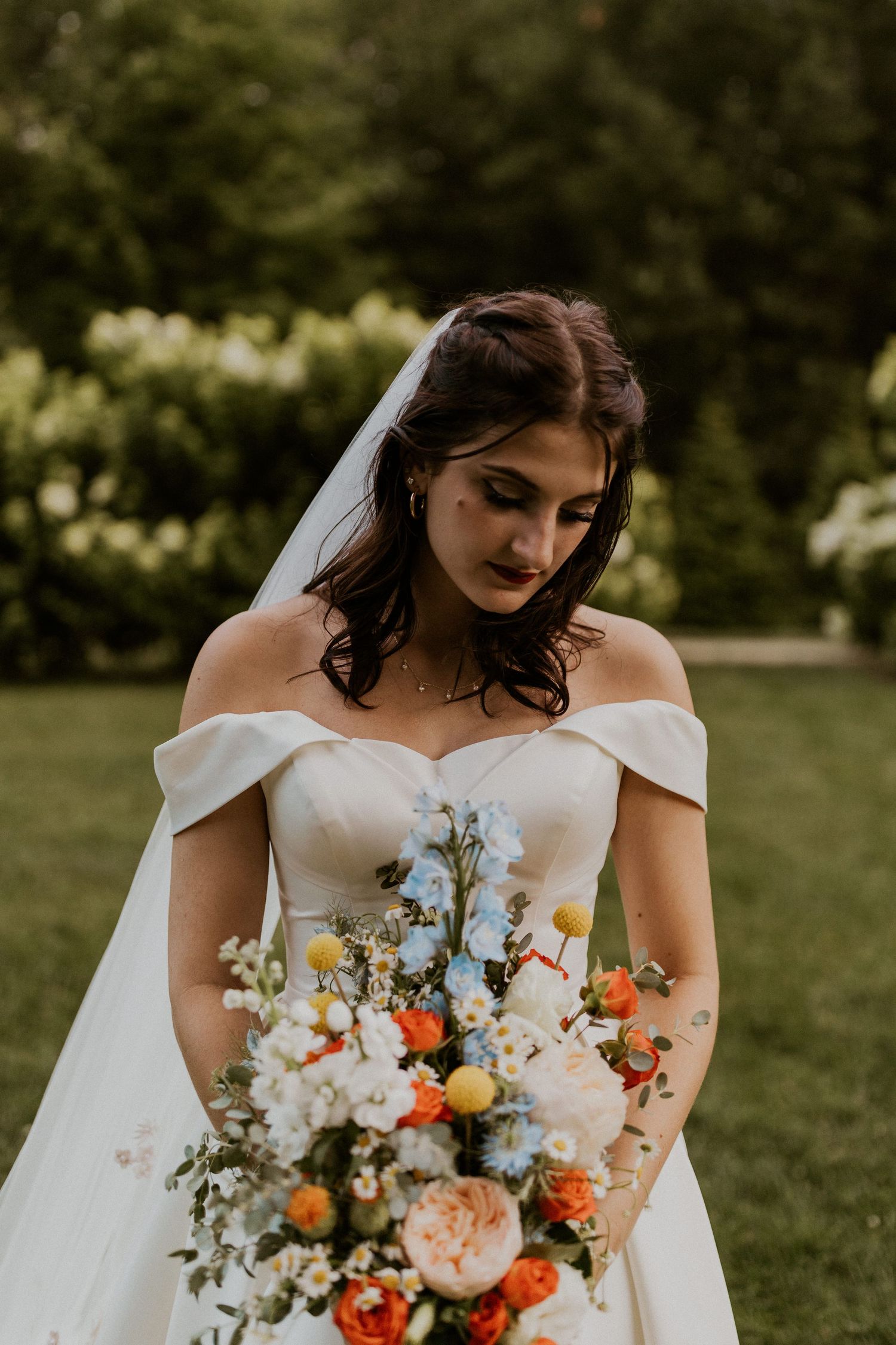 Bride holding vibrant orange and white wedding bouquet in elegant off-shoulder gown.